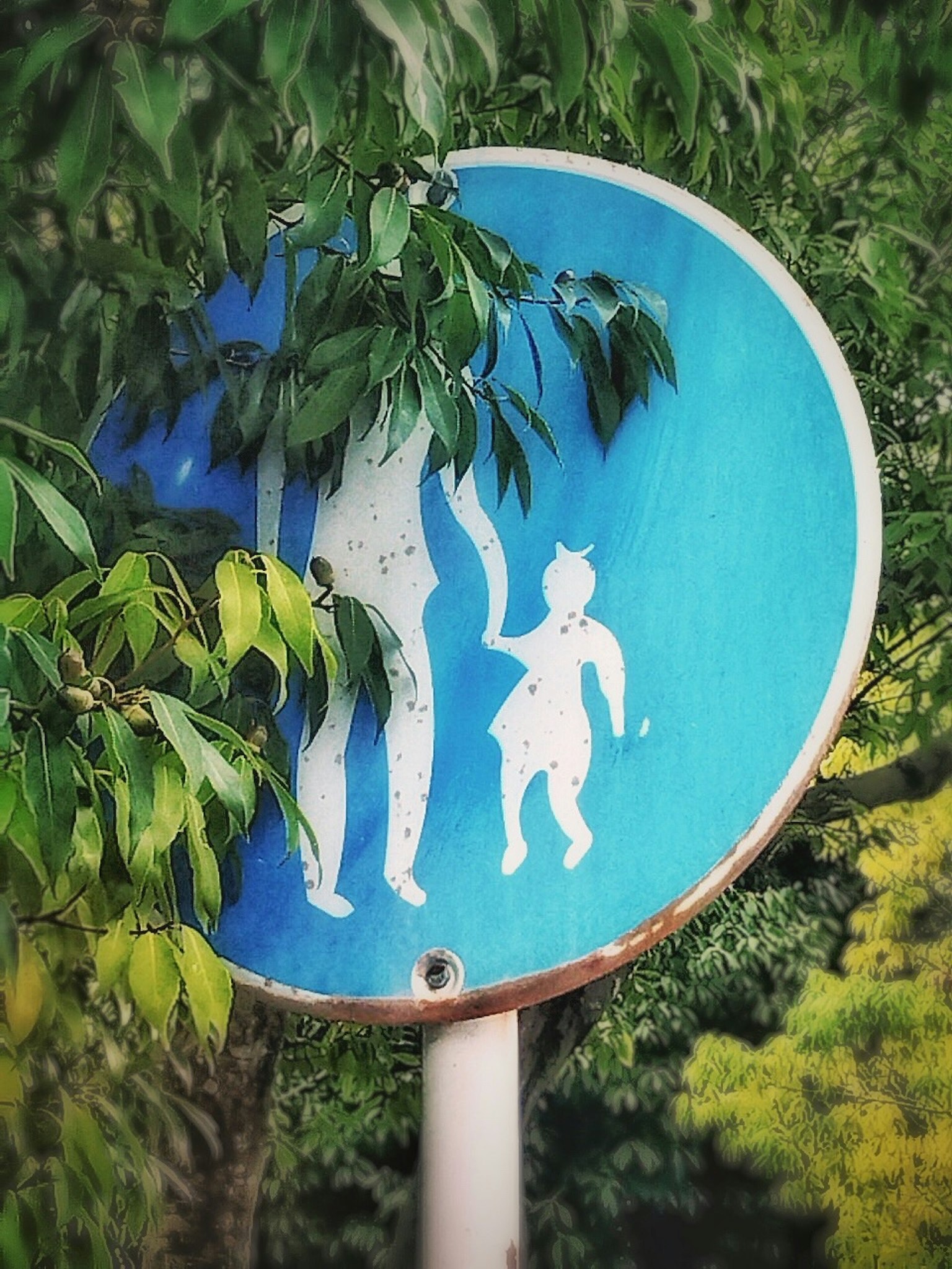 Una señal azul con siluetas de un adulto y un niño parcialmente cubiertas por hojas