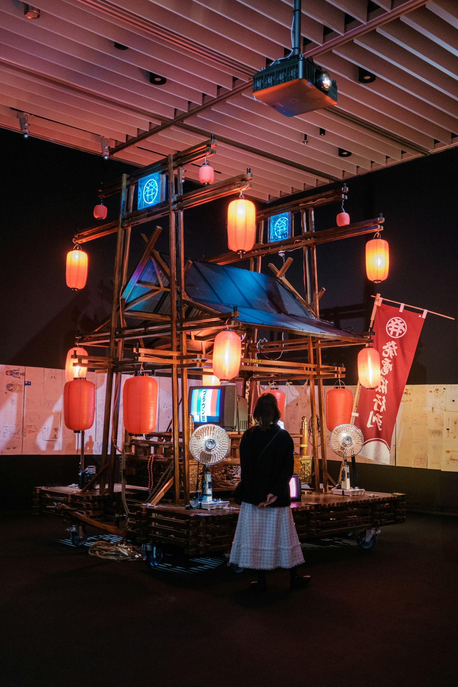 A bamboo structure adorned with red lanterns and blue fabric in an exhibition space