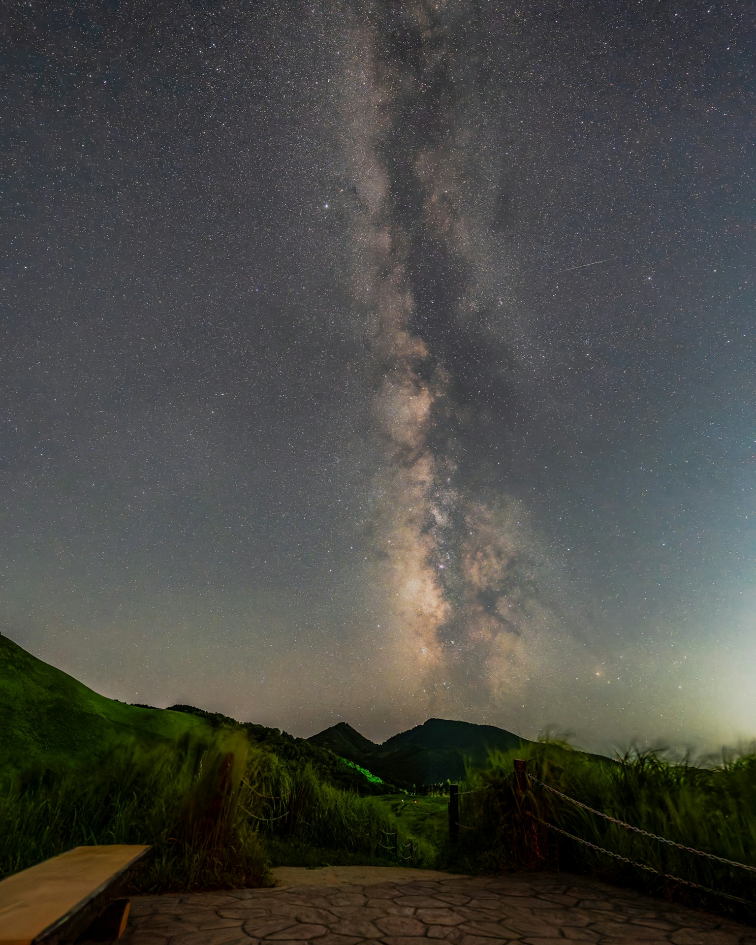 Vía Láctea extendiéndose por el cielo nocturno sobre colinas verdes