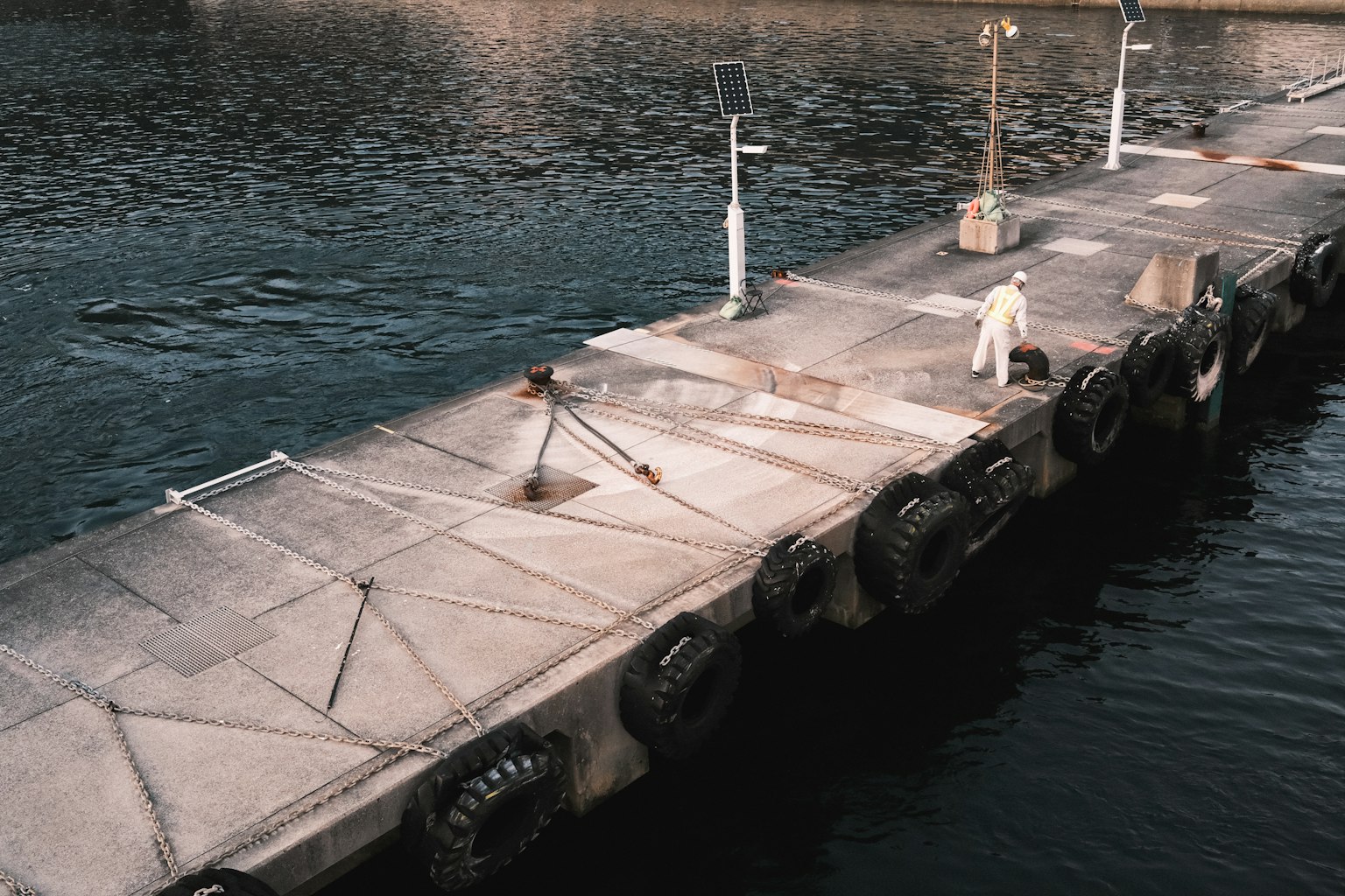 ท่าเรือคอนกรีตที่มียางลอยอยู่บนผิวน้ำและคนยืนอยู่