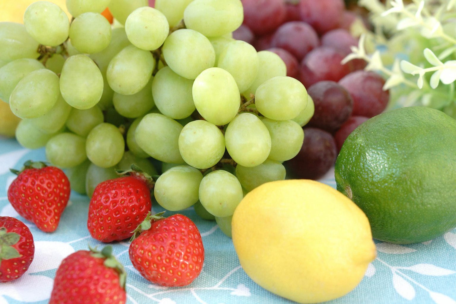 Un assortiment coloré de fruits comprenant des raisins verts des fraises rouges un citron jaune et un citron vert