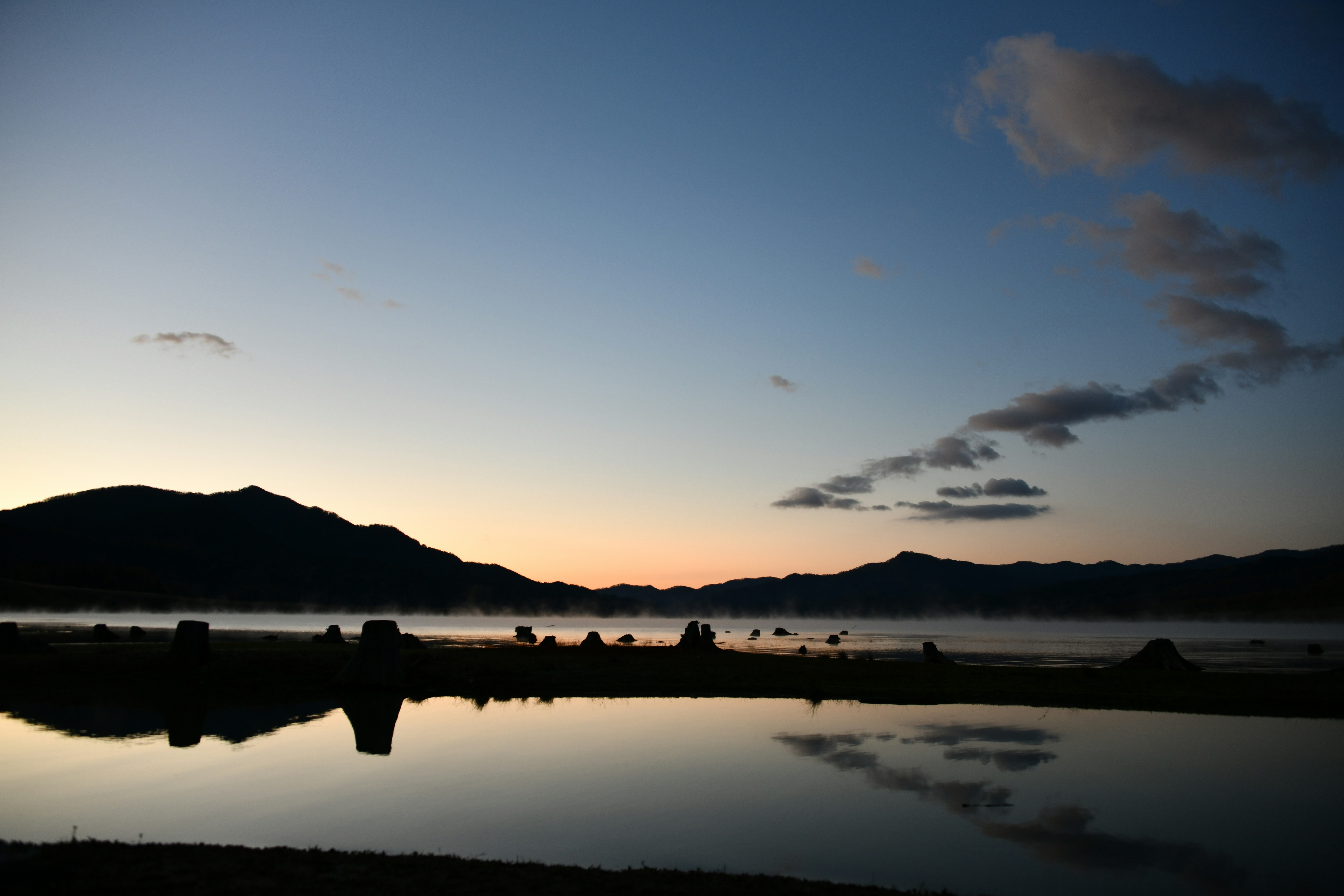 mountain silhouettes reflected on a calm lake at dusk
