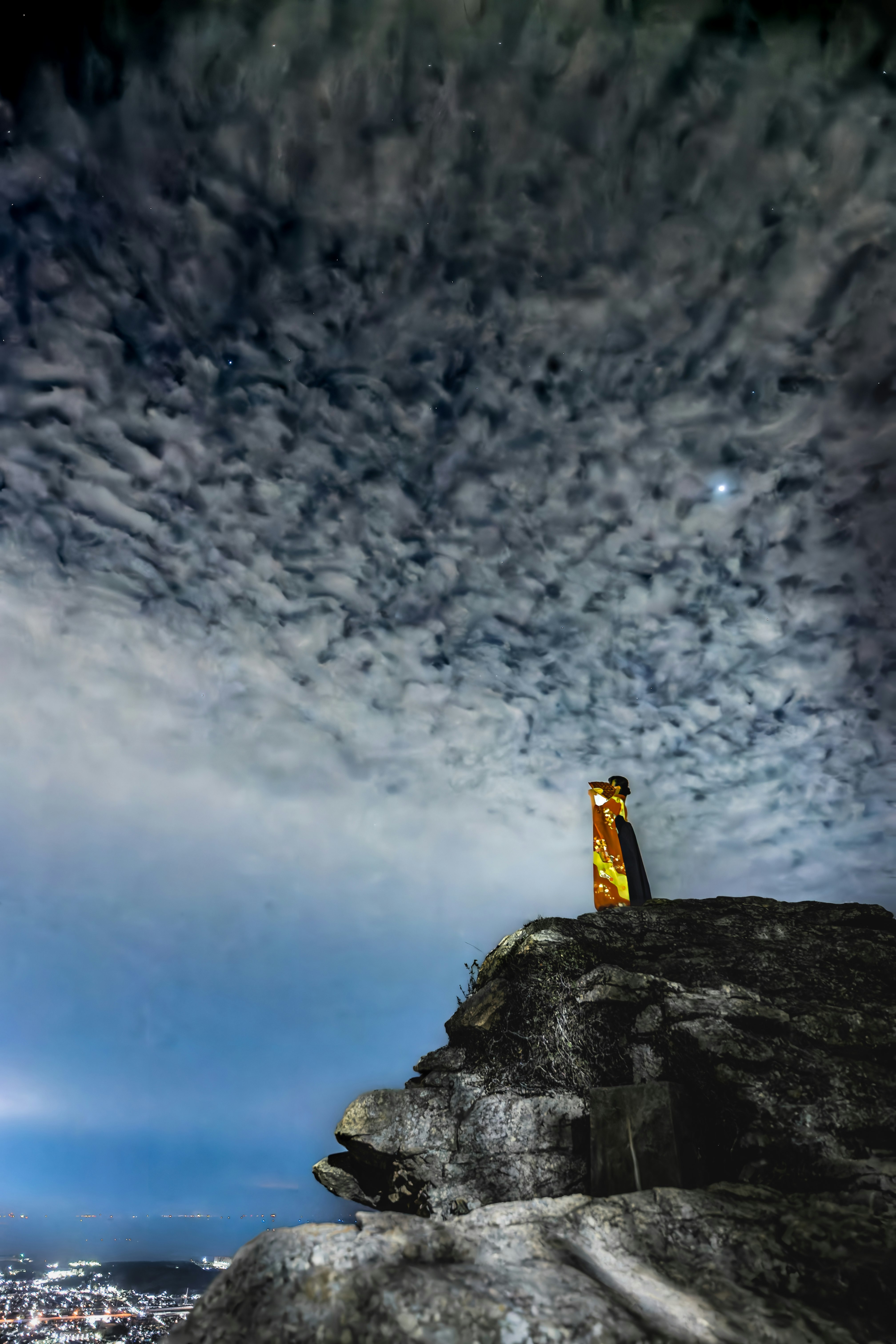 岩場の上に立つ人物と広がる夜景の空