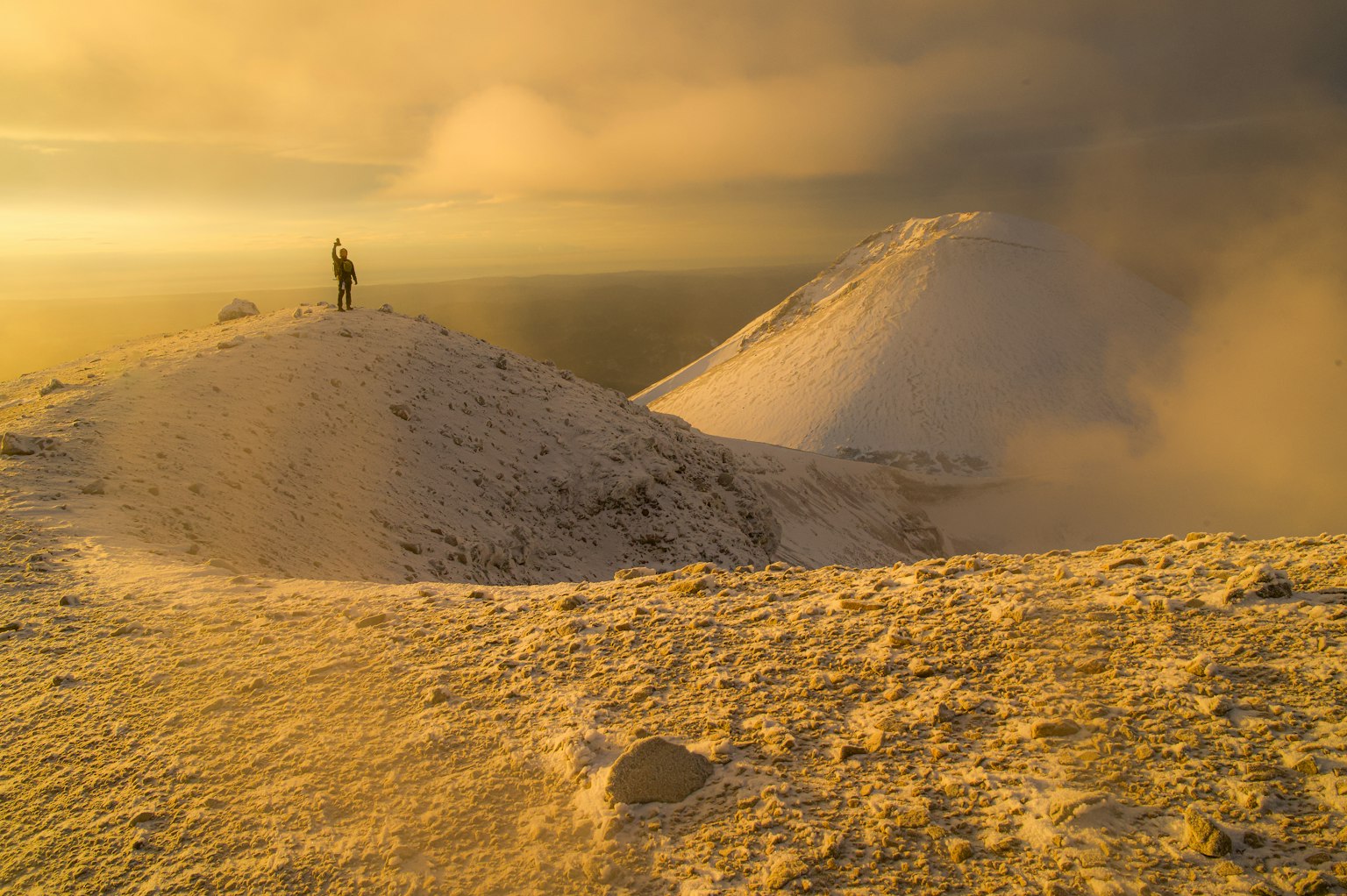 Eine Person steht auf einem schneebedeckten Berggipfel mit einer goldenen Landschaft