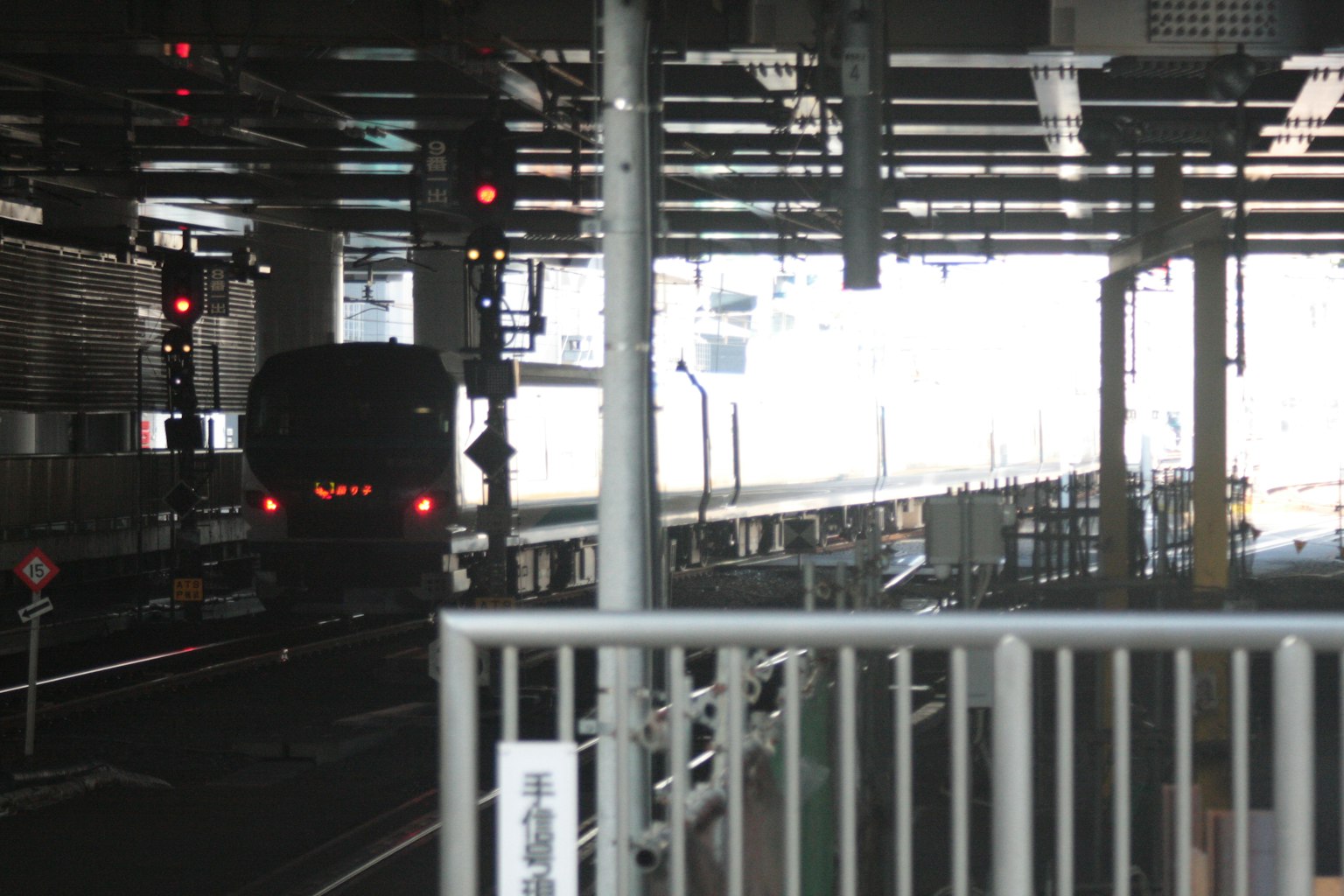 Train s'approchant de la plateforme sous des signaux rouges dans une gare