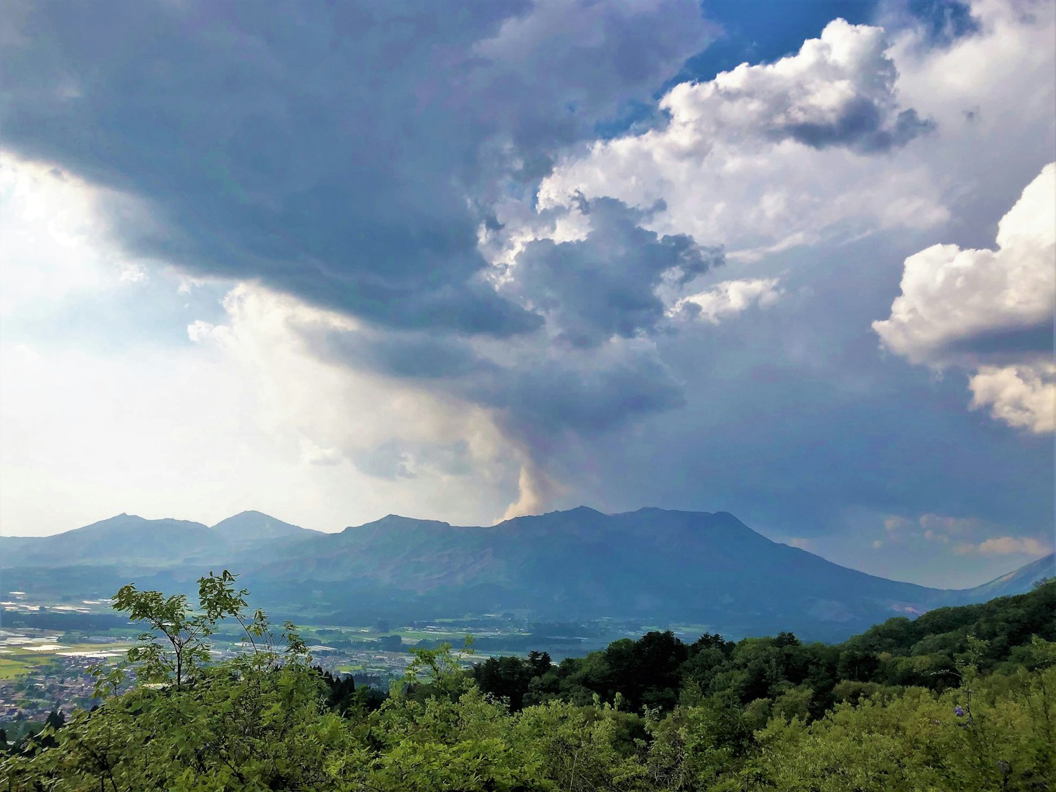 Pemandangan gunung berapi yang mengeluarkan asap dengan latar belakang pegunungan dan awan