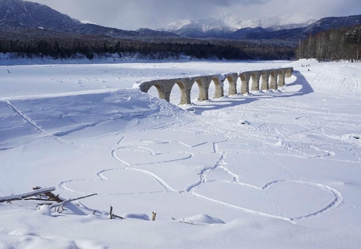 Eine verschneite Landschaft mit einem Fluss und einer Bogenbrücke