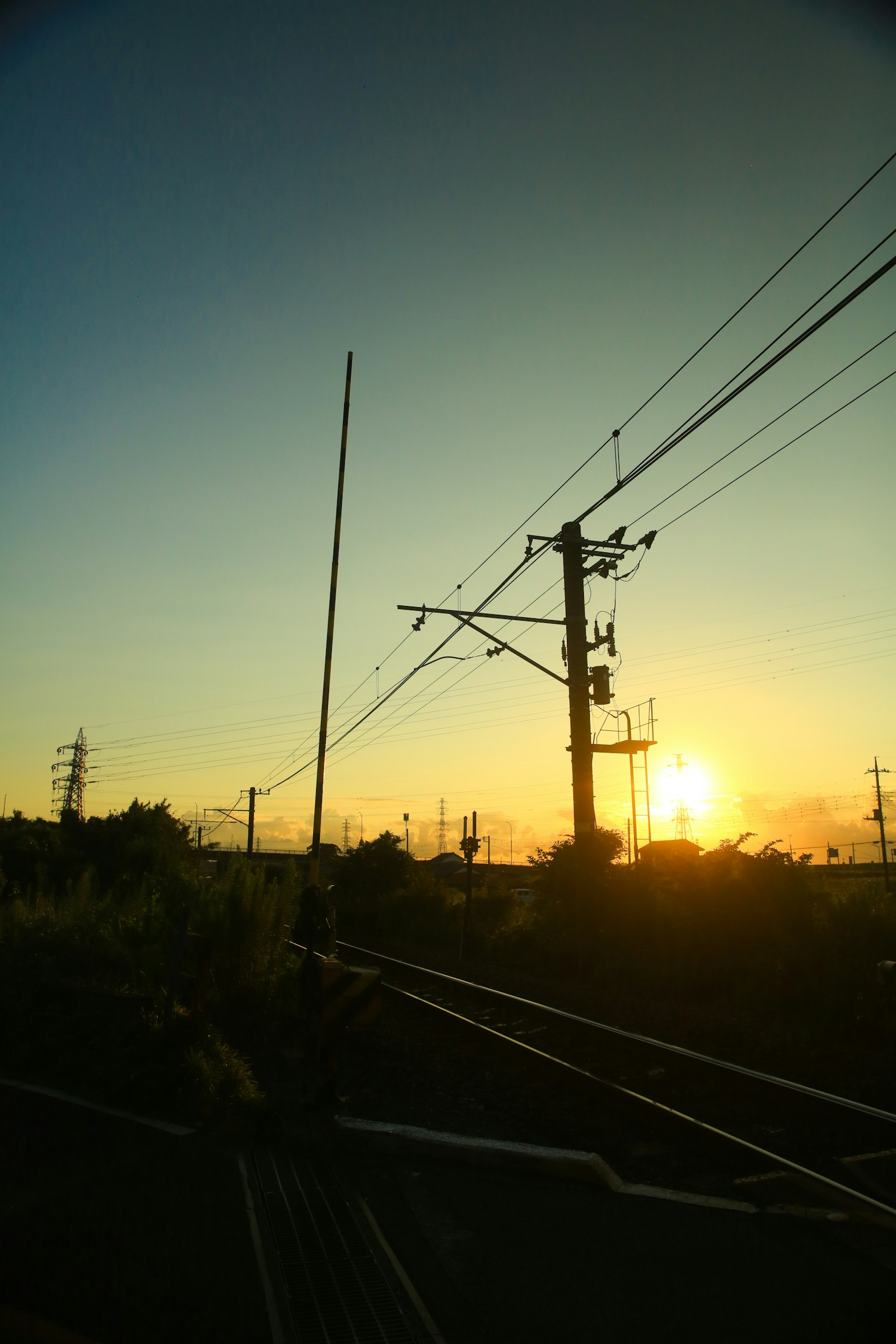 Silhouette of railway overhead lines and utility poles against a sunset sky