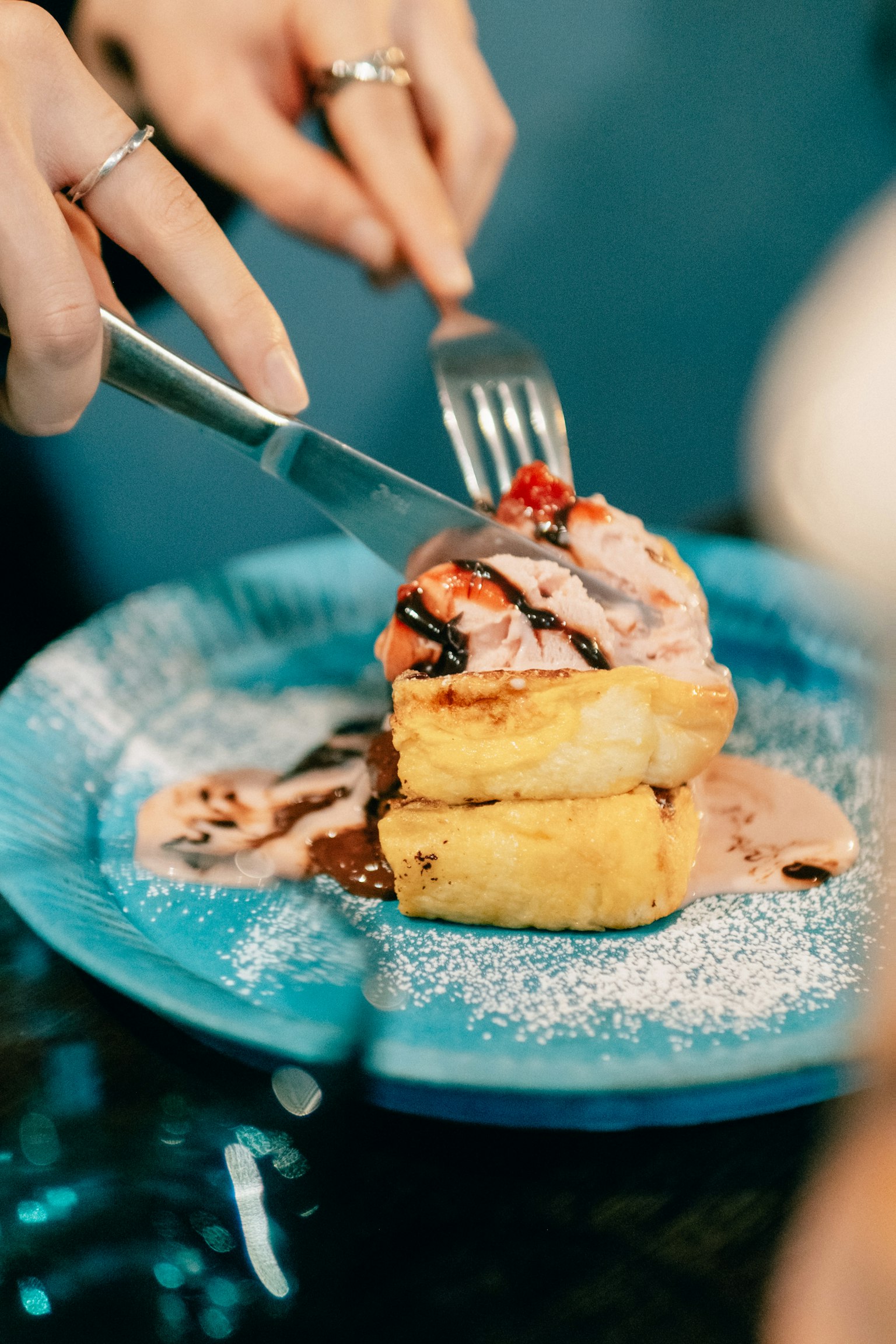 A person holding a fork and knife cutting into a dessert topped with ice cream and sauce