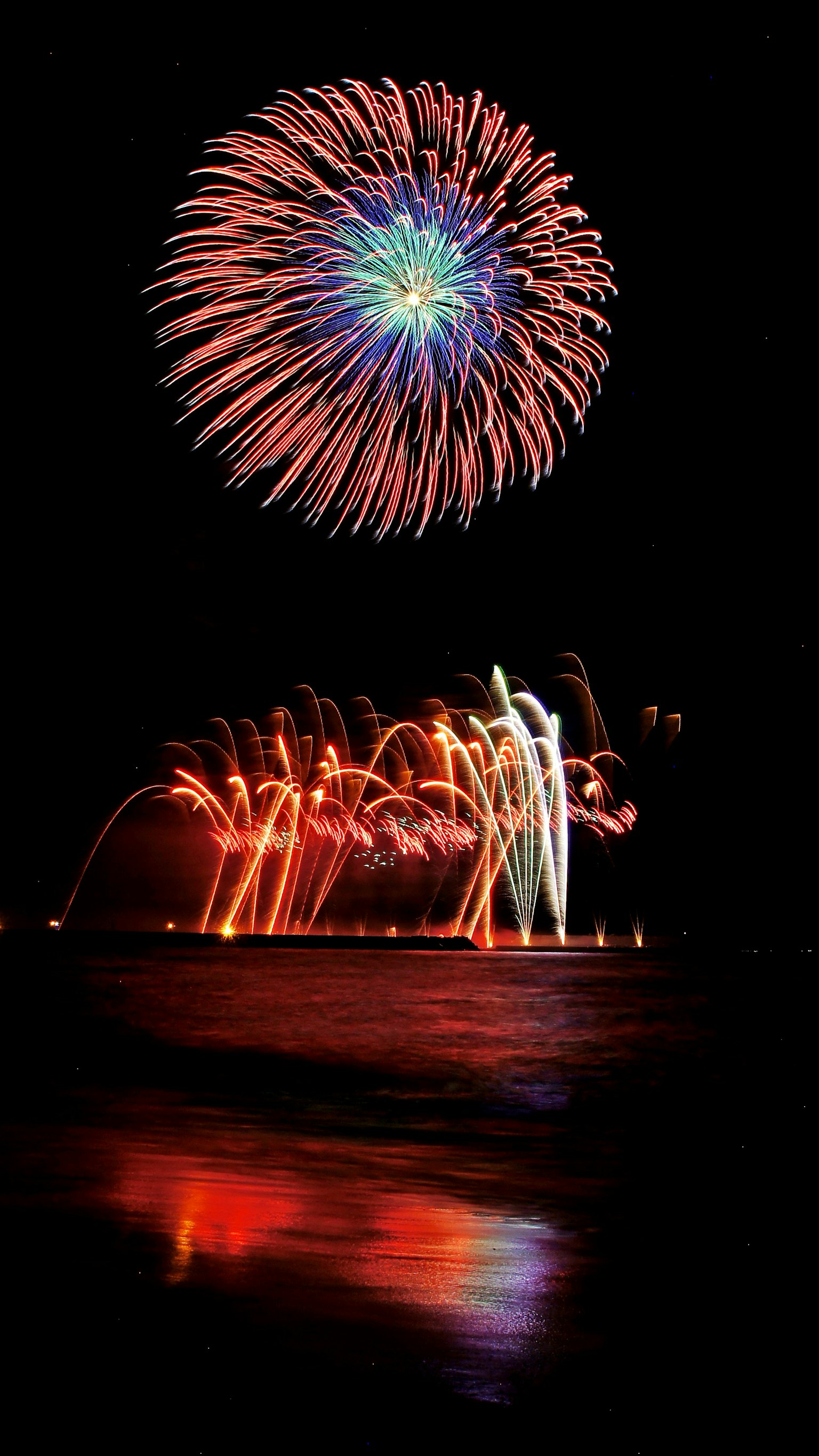 Bunte Feuerwerke, die am Nachthimmel explodieren, mit Reflexionen auf dem Wasser