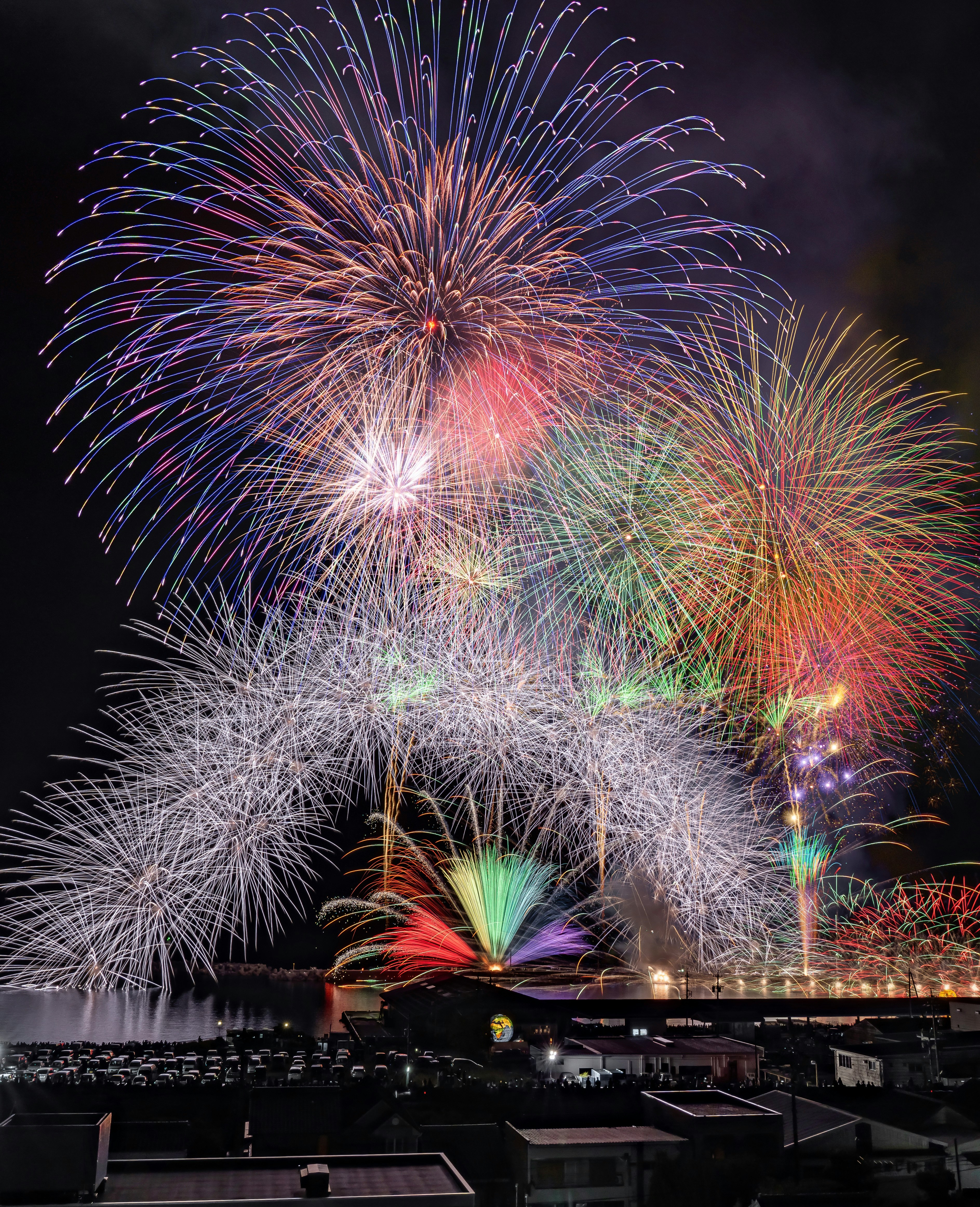夜空に咲くカラフルな花火と観客席のある会場の風景