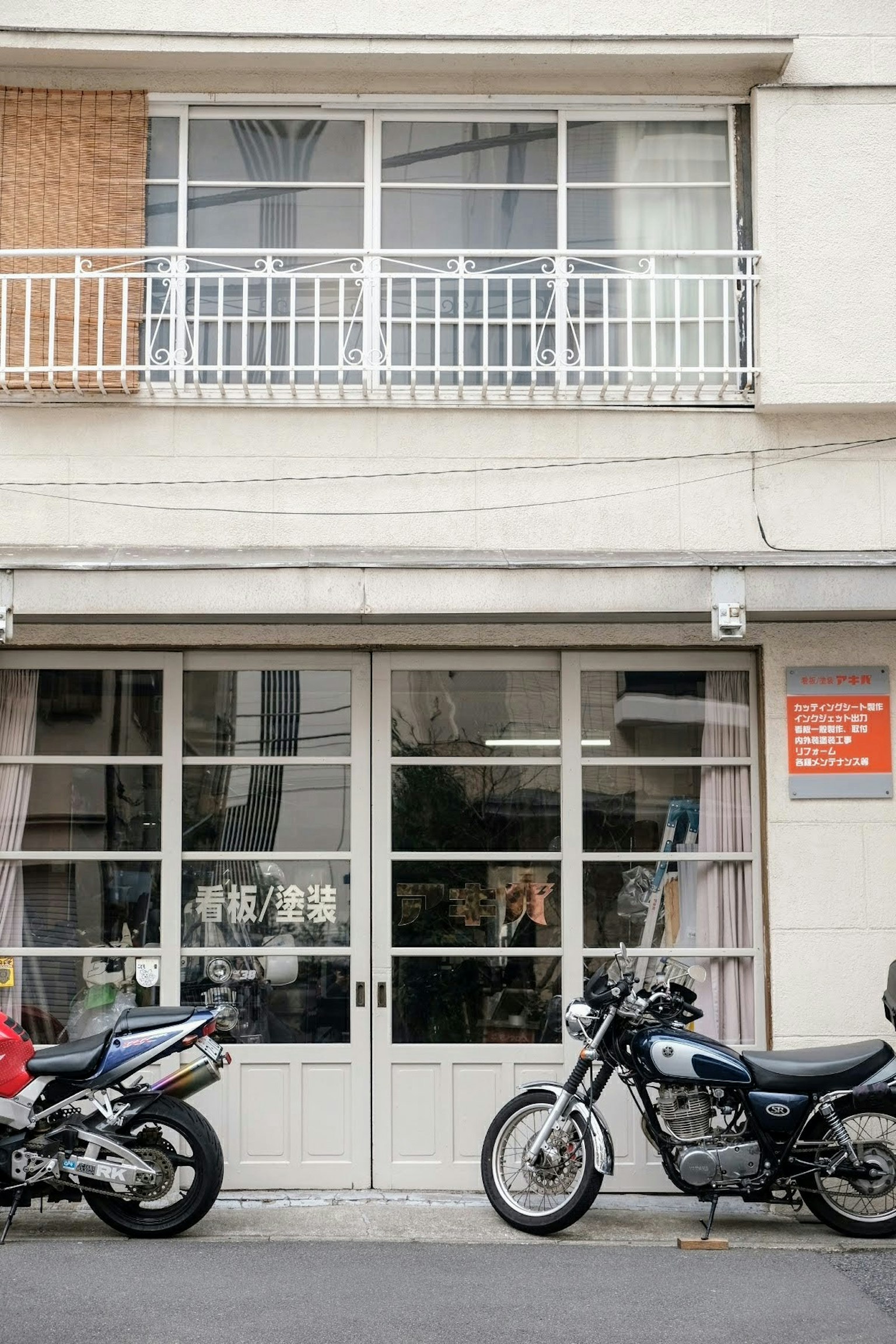 Two motorcycles parked in front of a white building with large windows