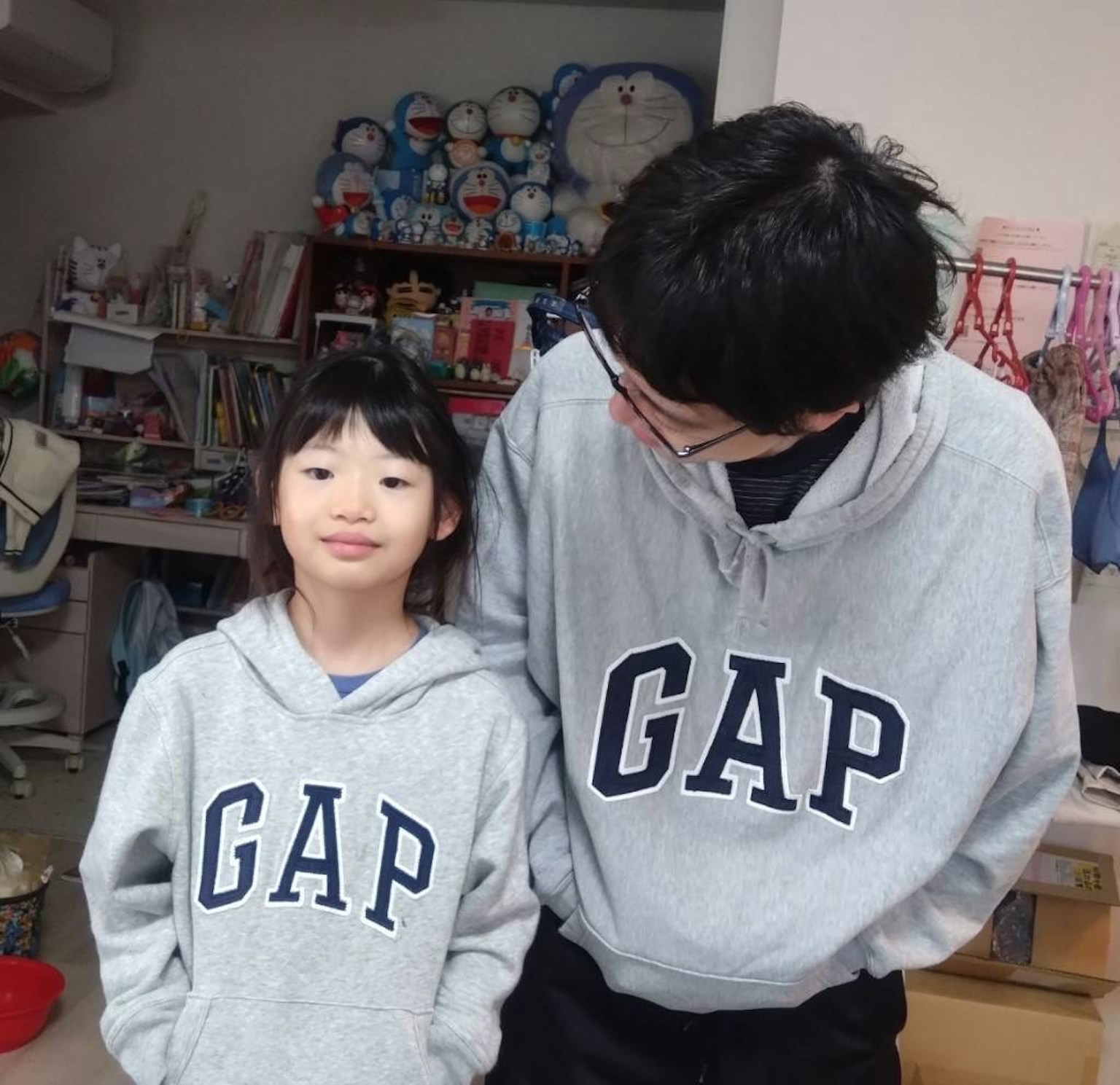 A child and an adult wearing gray GAP hoodies smiling indoors