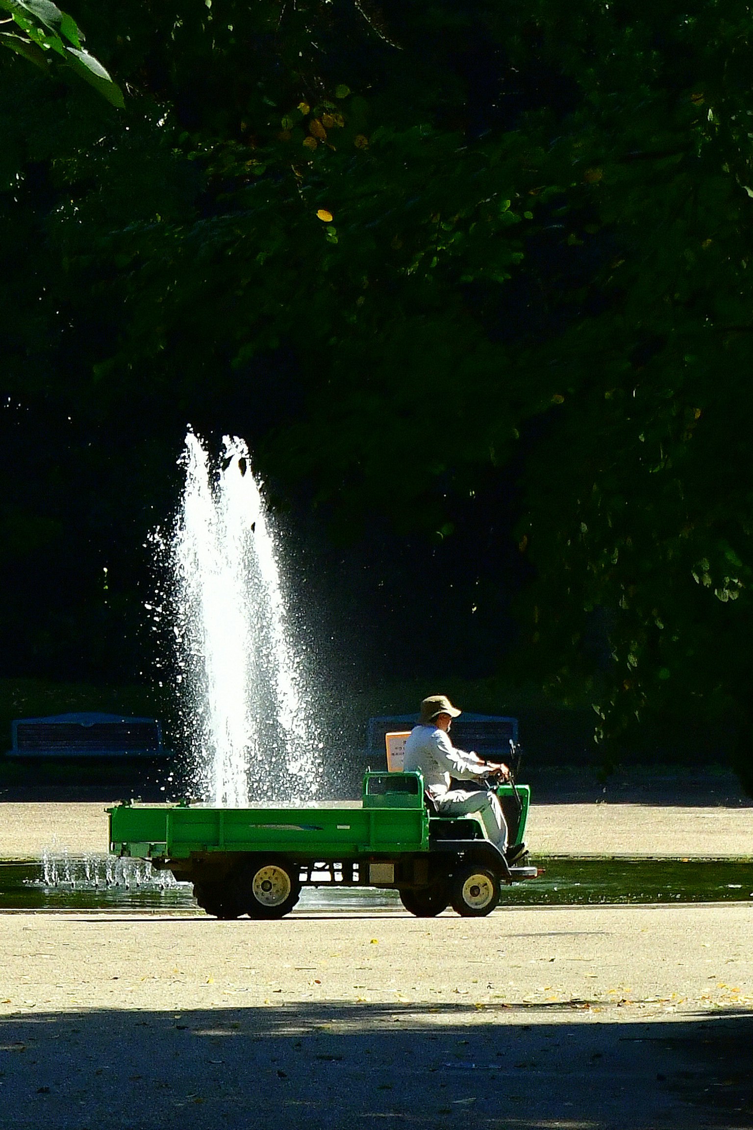 公園で緑のトラクターを運転する作業員と噴水