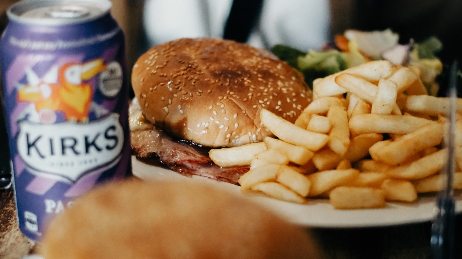 Ein Teller mit einem Hamburger und Pommes frites neben einer Dose Kirks