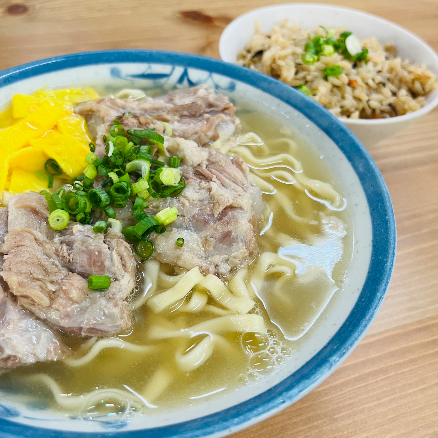 Một bát súp với thịt và mì bên cạnh một đĩa cơm nhỏ