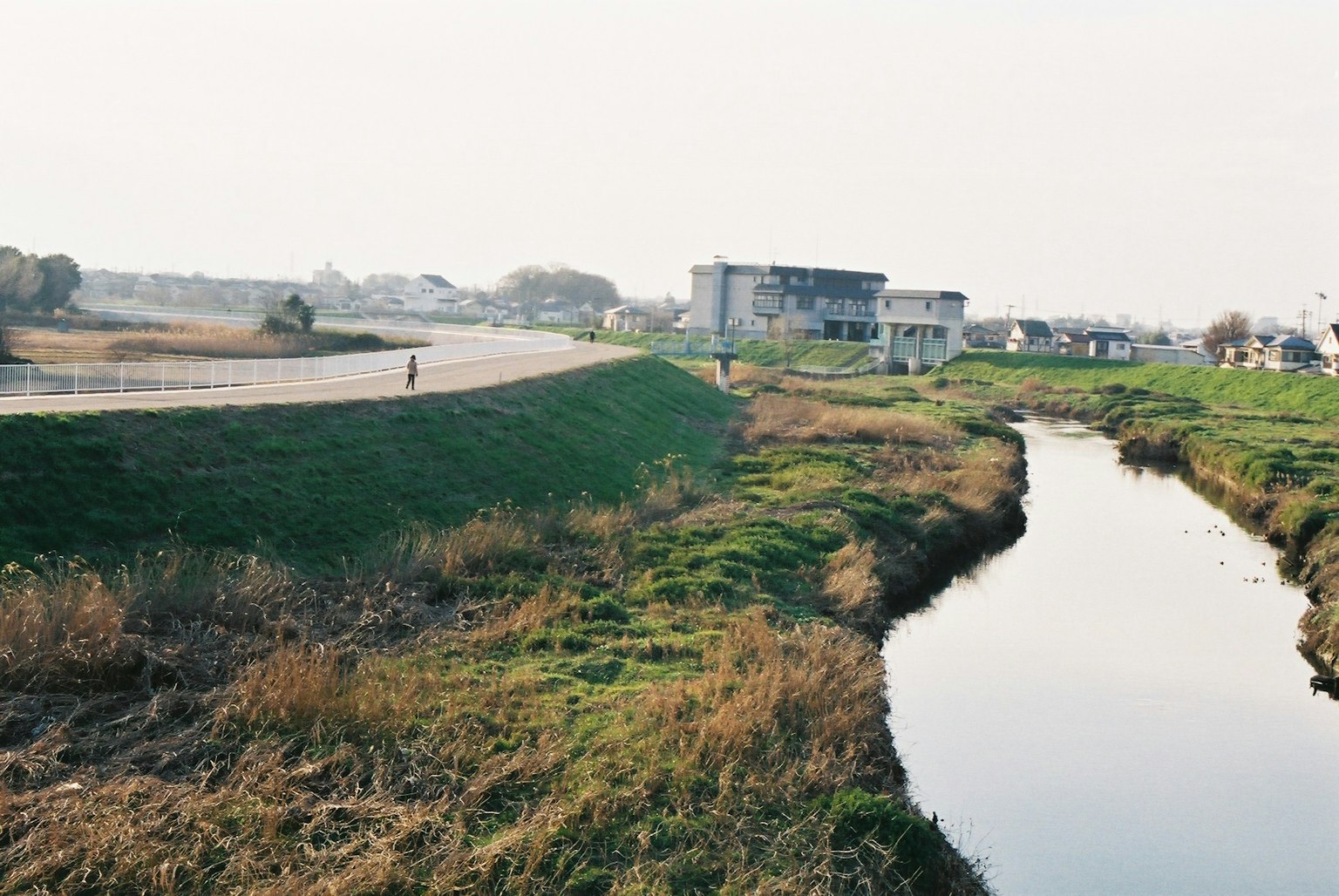 Un paysage avec une rivière et des zones herbeuses avec un bâtiment en arrière-plan