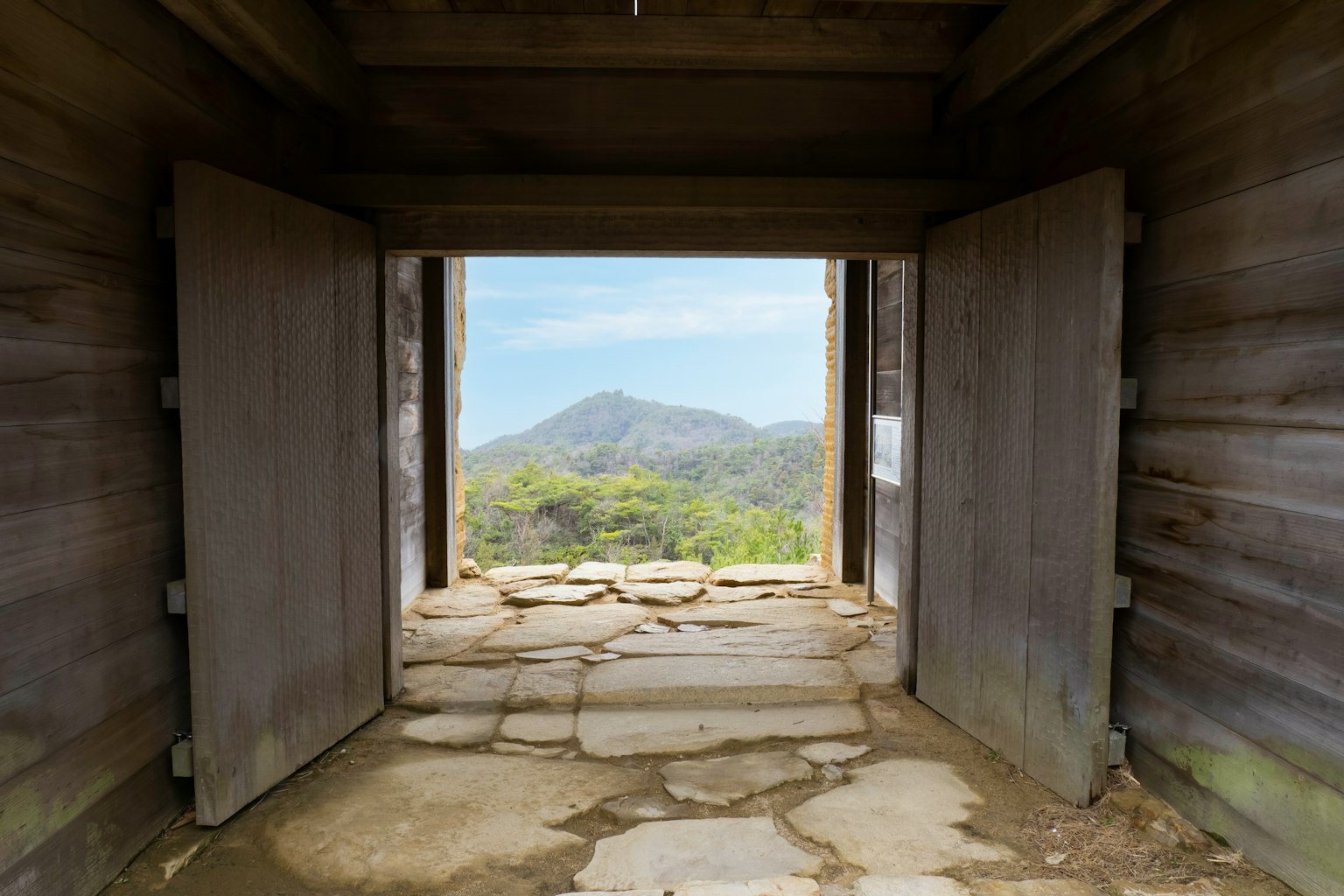 Interno di un vecchio edificio con porte di legno che rivelano una vista montana