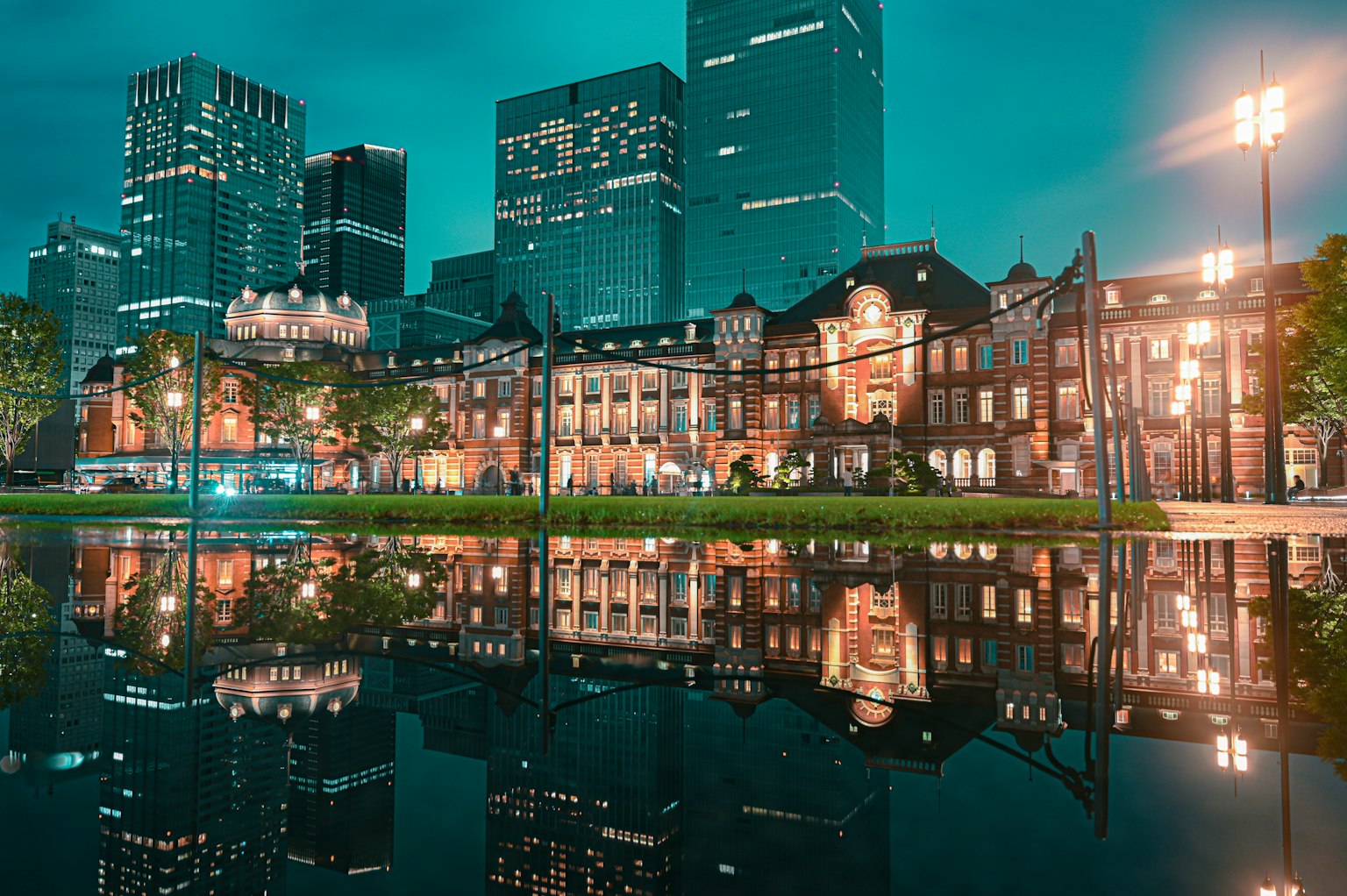 Pemandangan malam yang indah dari Stasiun Tokyo dengan gedung pencakar langit modern dan bangunan bersejarah yang terpantul di air
