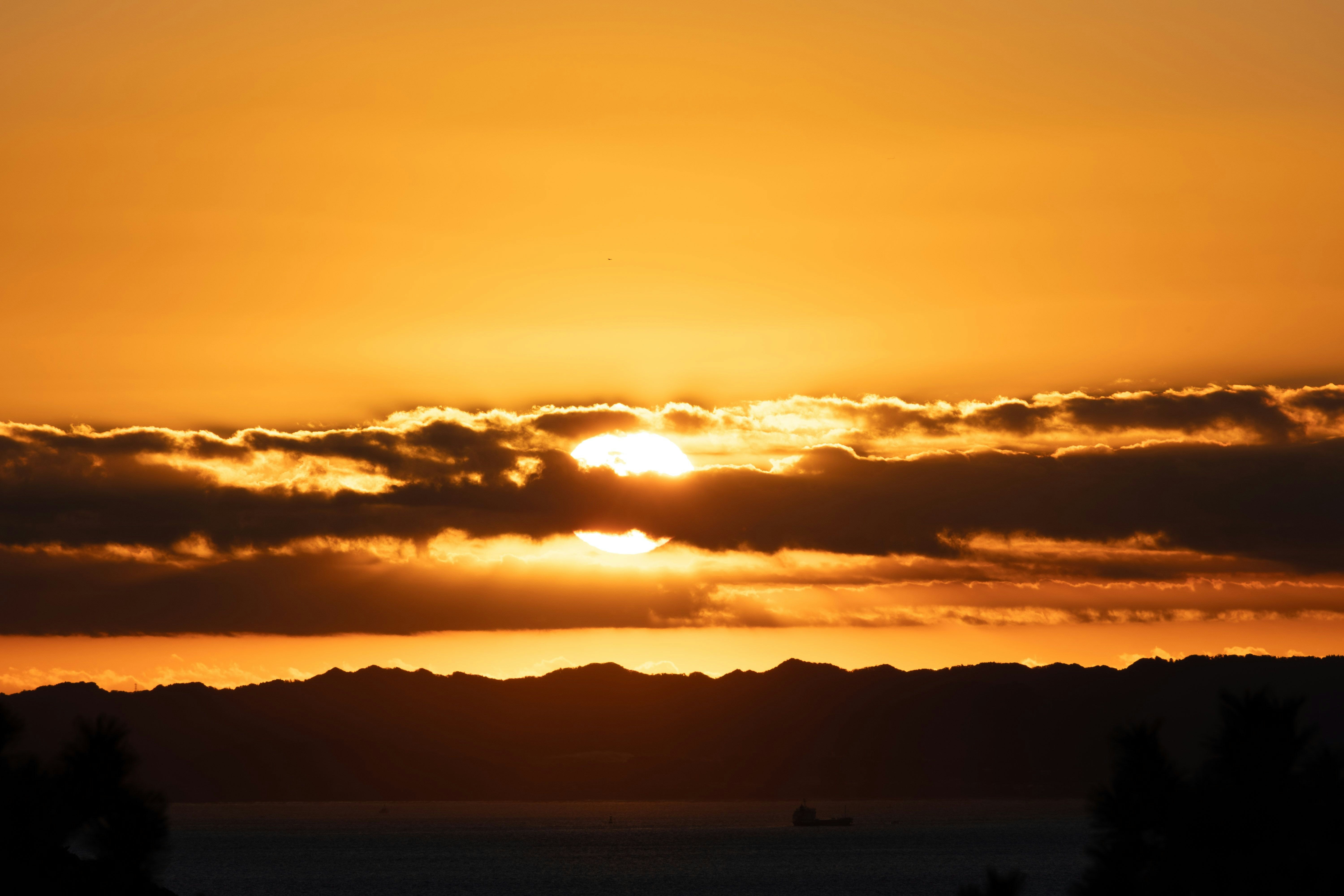 夕日を雲の隙間からのぞかせる海辺の水平線