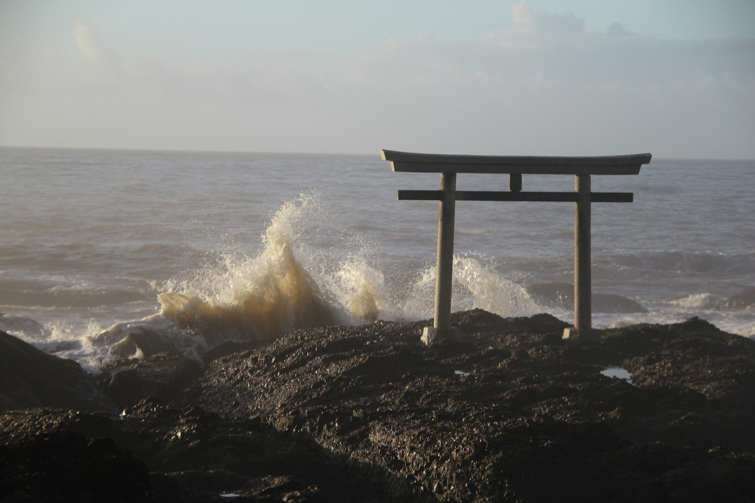 Torii faisant face à la mer avec des vagues s'écrasant sur les rochers