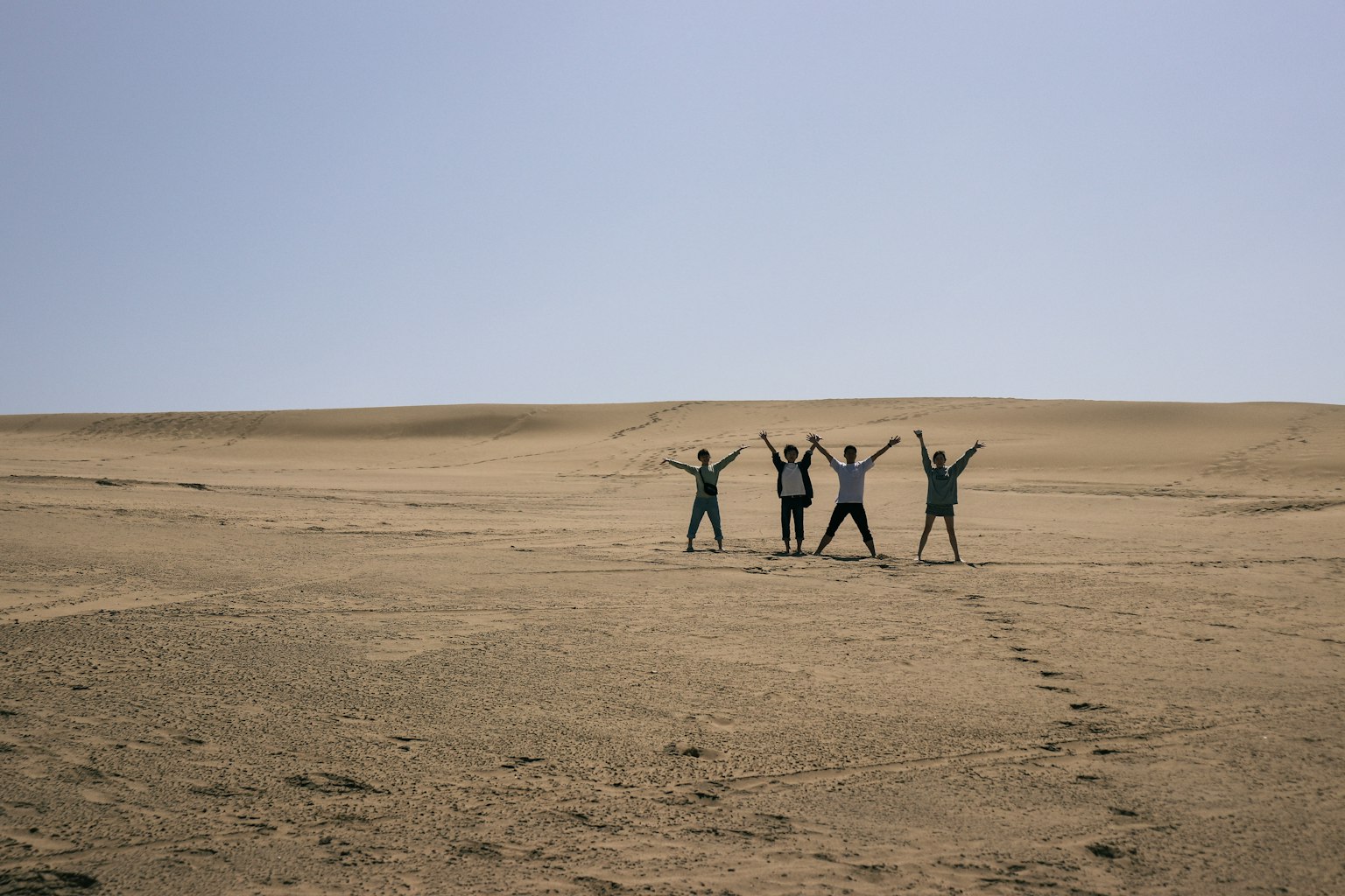 Quatre personnes posant sur un paysage de sable avec les bras levés