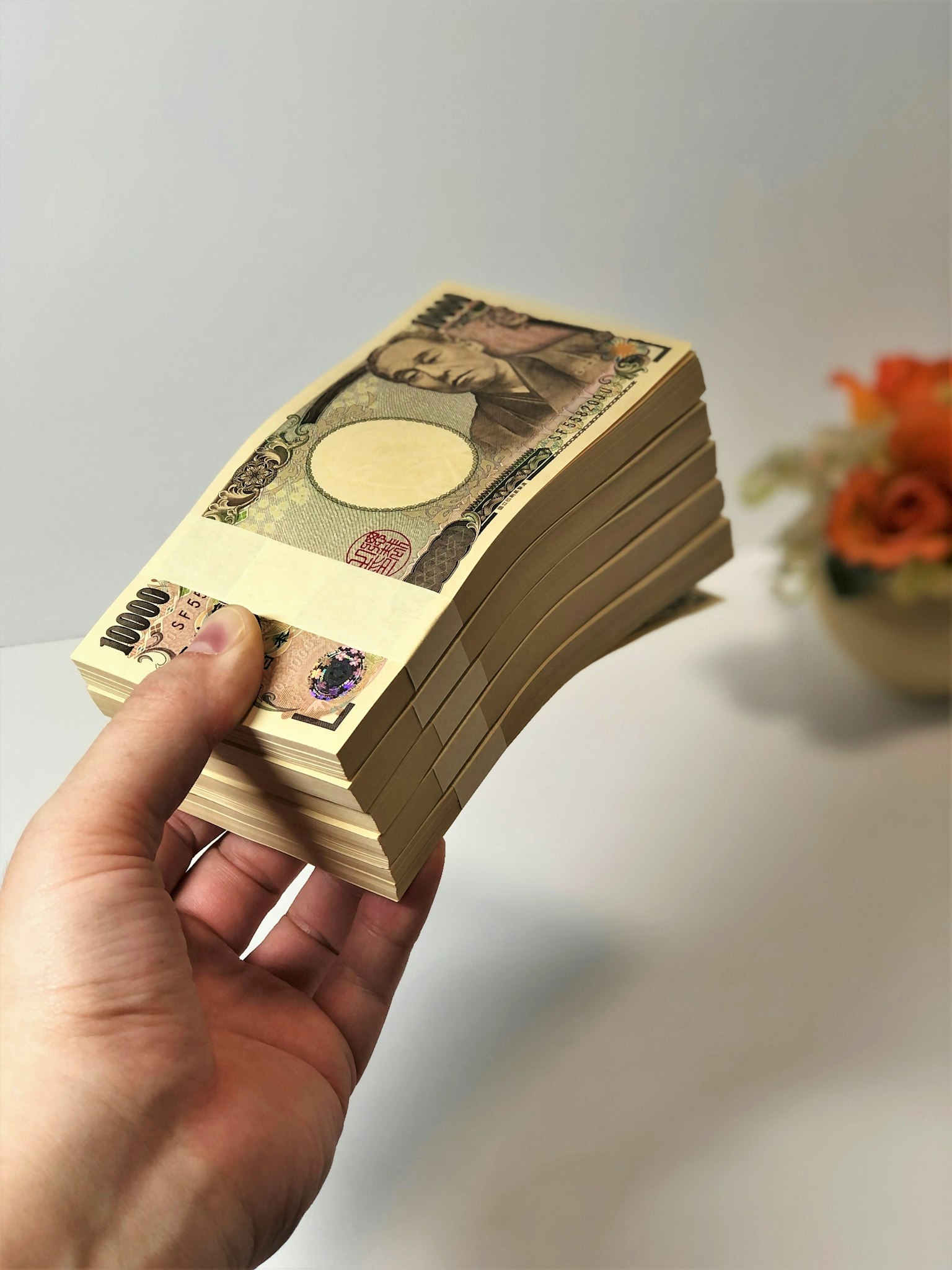 A hand holding a stack of Japanese yen with a floral background