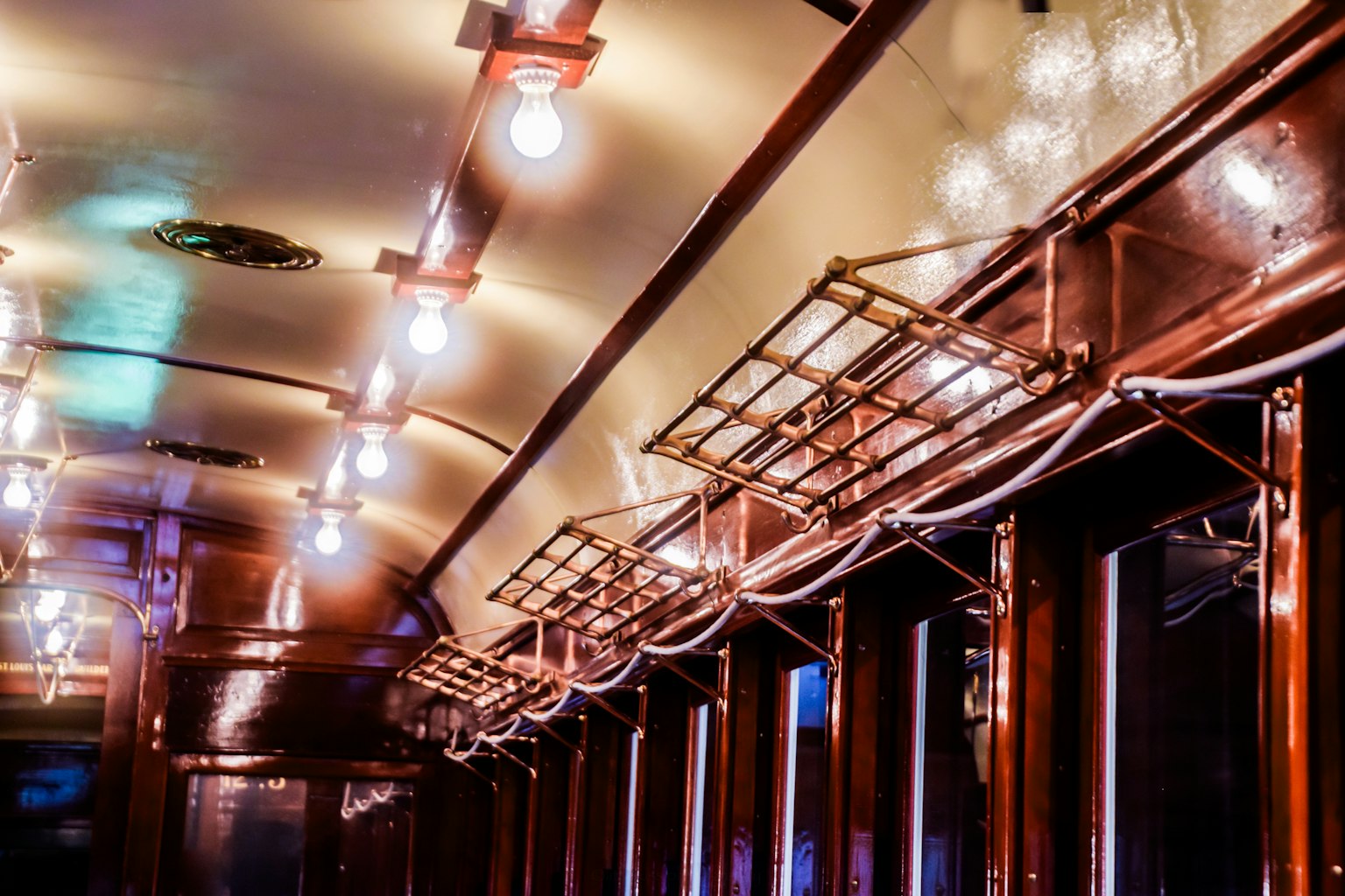 Interior of a vintage train car featuring wooden window frames bright lamps and metal hangers