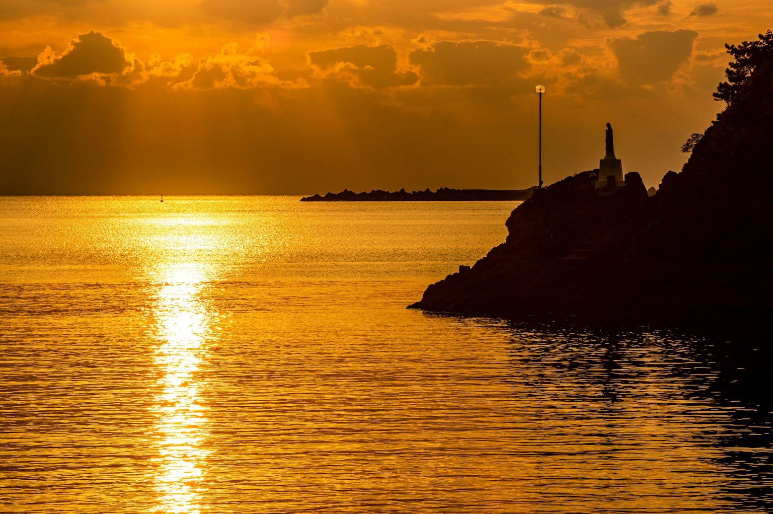 Beautiful scenery of sunset reflecting on the sea with a rocky shore and lighthouse