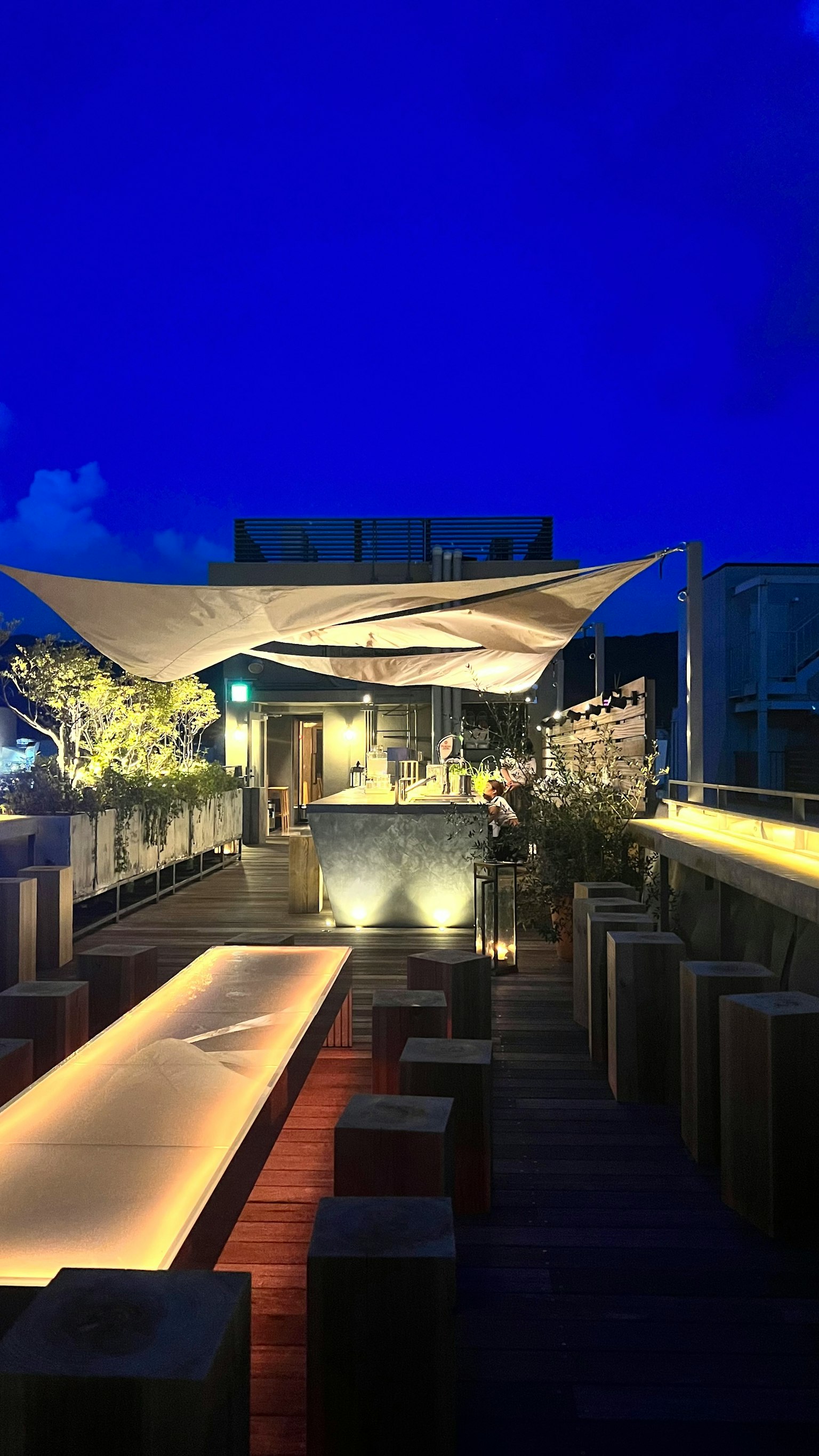 Terraza exterior moderna bajo un cielo nocturno con mesas y sillas iluminadas