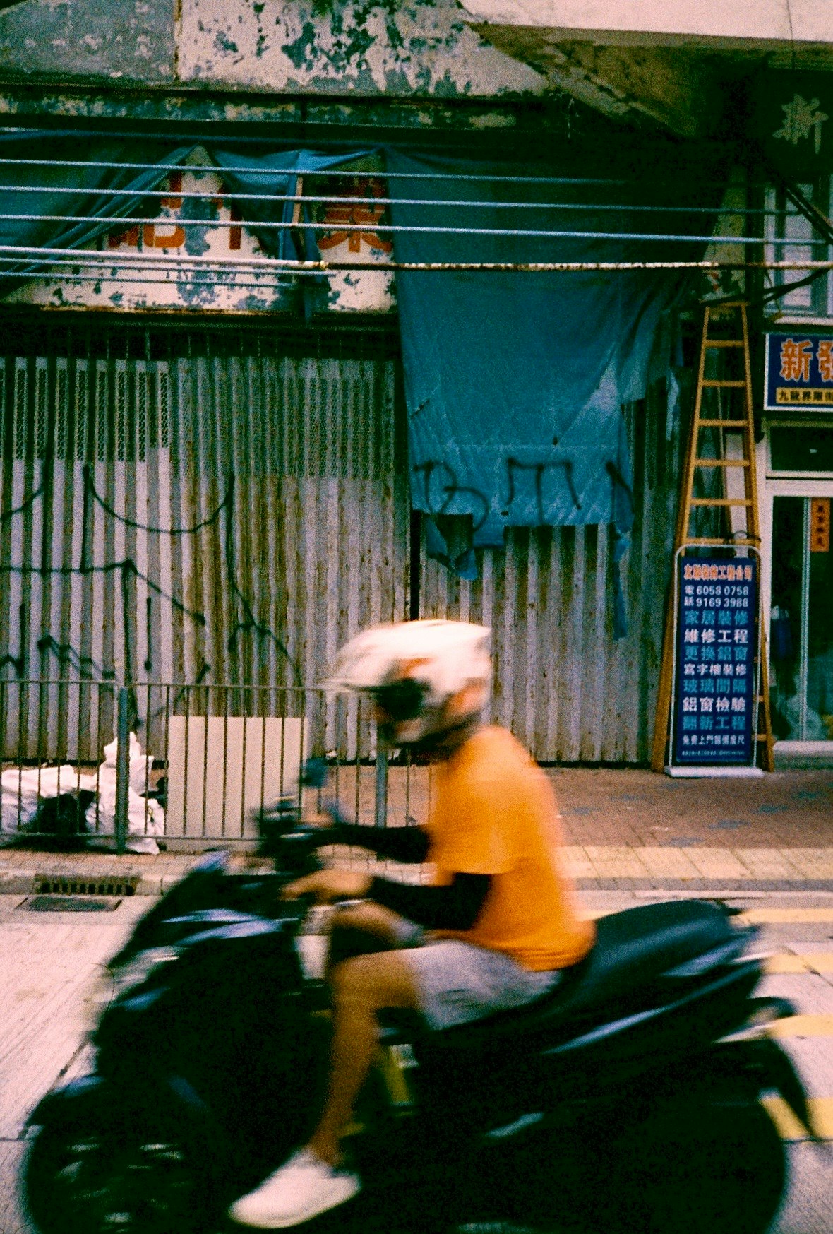 주황색 셔츠를 입은 라이더가 검은색 오토바이를 타고 있으며 배경에는 파란색 천과 낡은 벽이 보인다