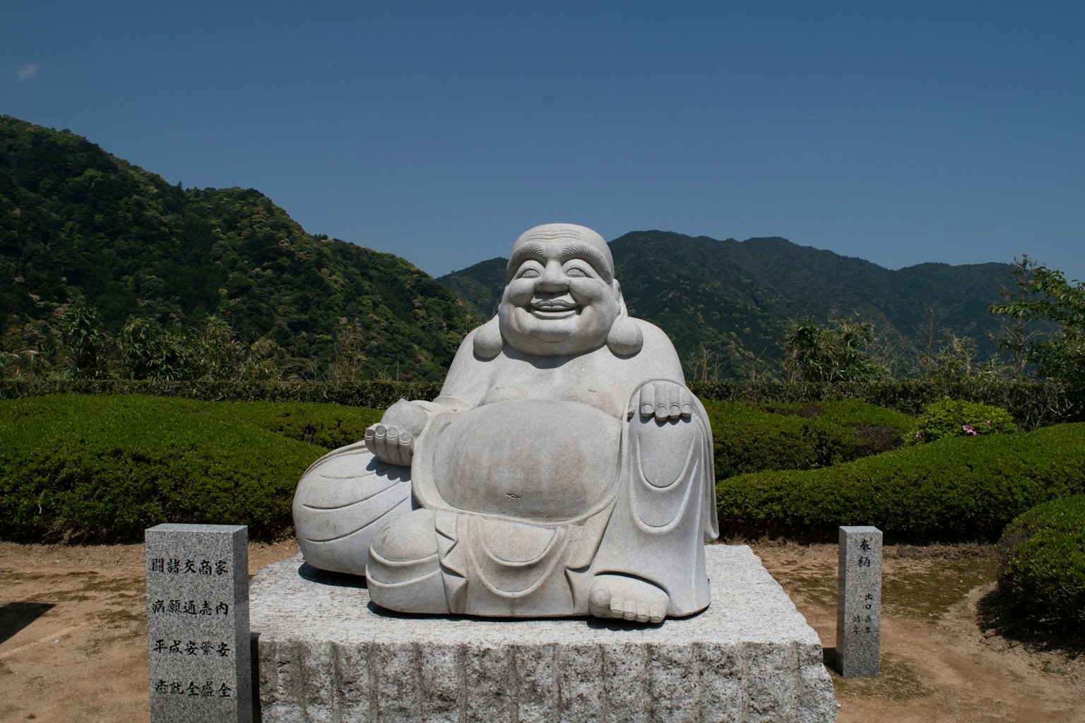 Une statue blanche d'un Bouddha rieur assis devant un paysage montagneux