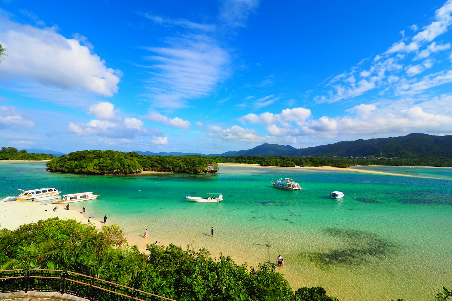 Spiaggia panoramica con acqua turchese chiara e barche sotto un cielo blu