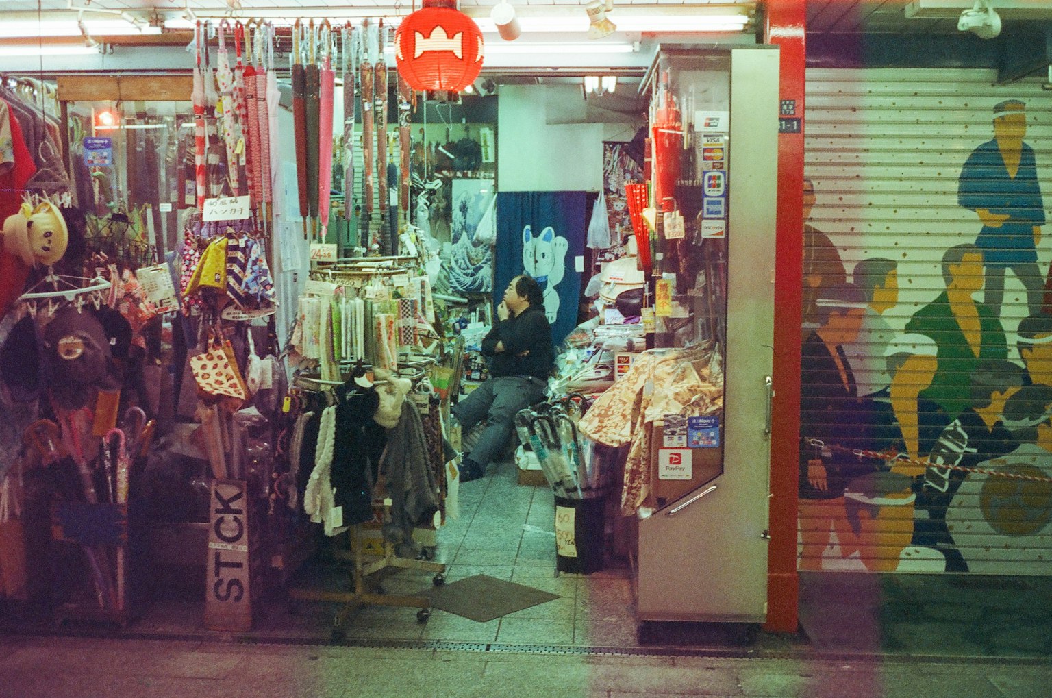 Entrée d'un marché de rue animé avec des magasins affichant des vêtements et des accessoires une personne assise à l'arrière-plan