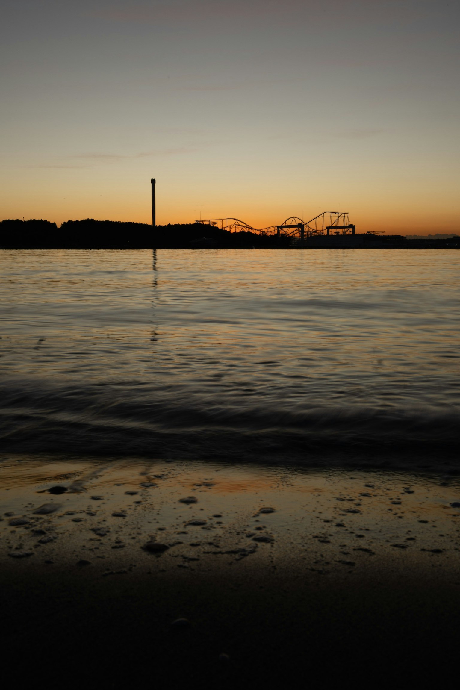 Küstenansicht bei Sonnenuntergang mit Reflexionen im Wasser Silhouette eines Vergnügungsparks in der Ferne
