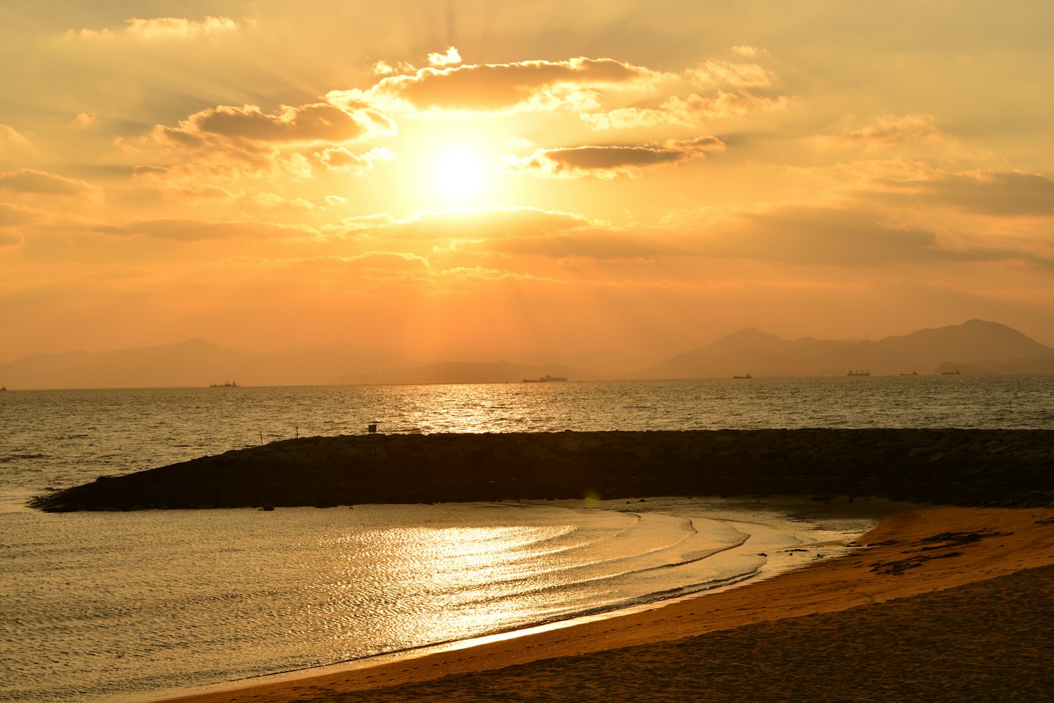 ทิวทัศน์พระอาทิตย์ตกที่สวยงามเหนือทะเลพร้อมคลื่นที่ชายหาดและเขื่อนกันคลื่น