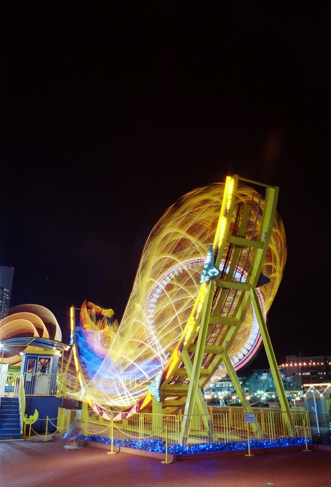夜の遊園地で光の軌跡が描かれる回転遊具のある風景