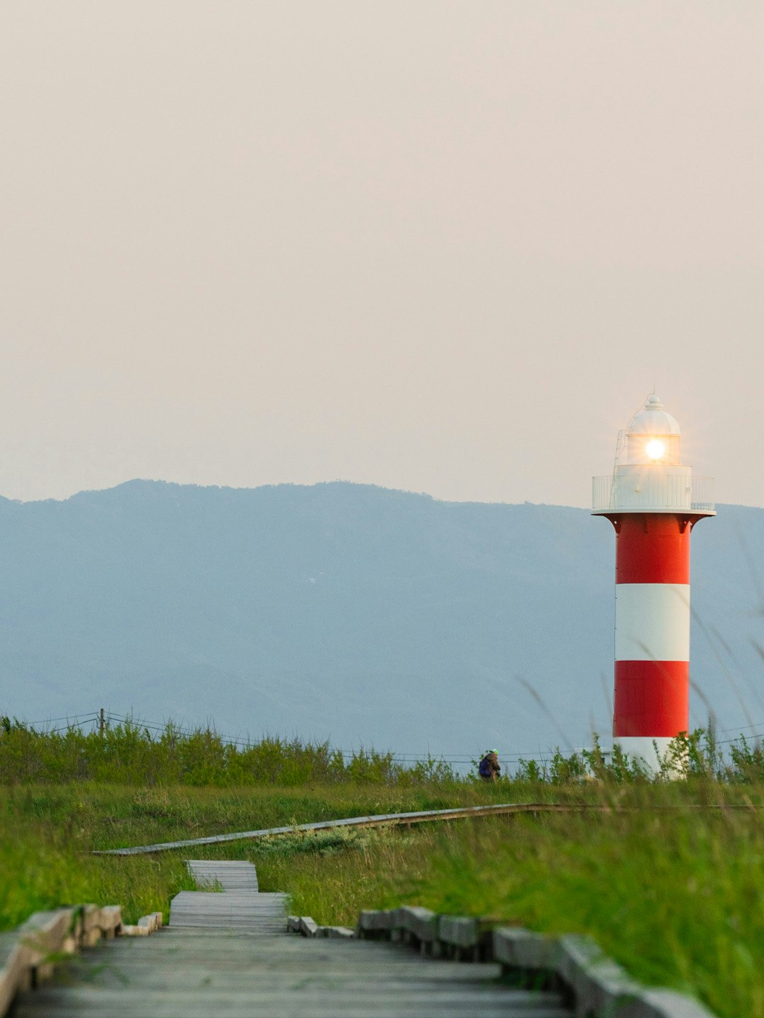 灯台と芝生の小道、遠くに山並みが見える海辺の風景