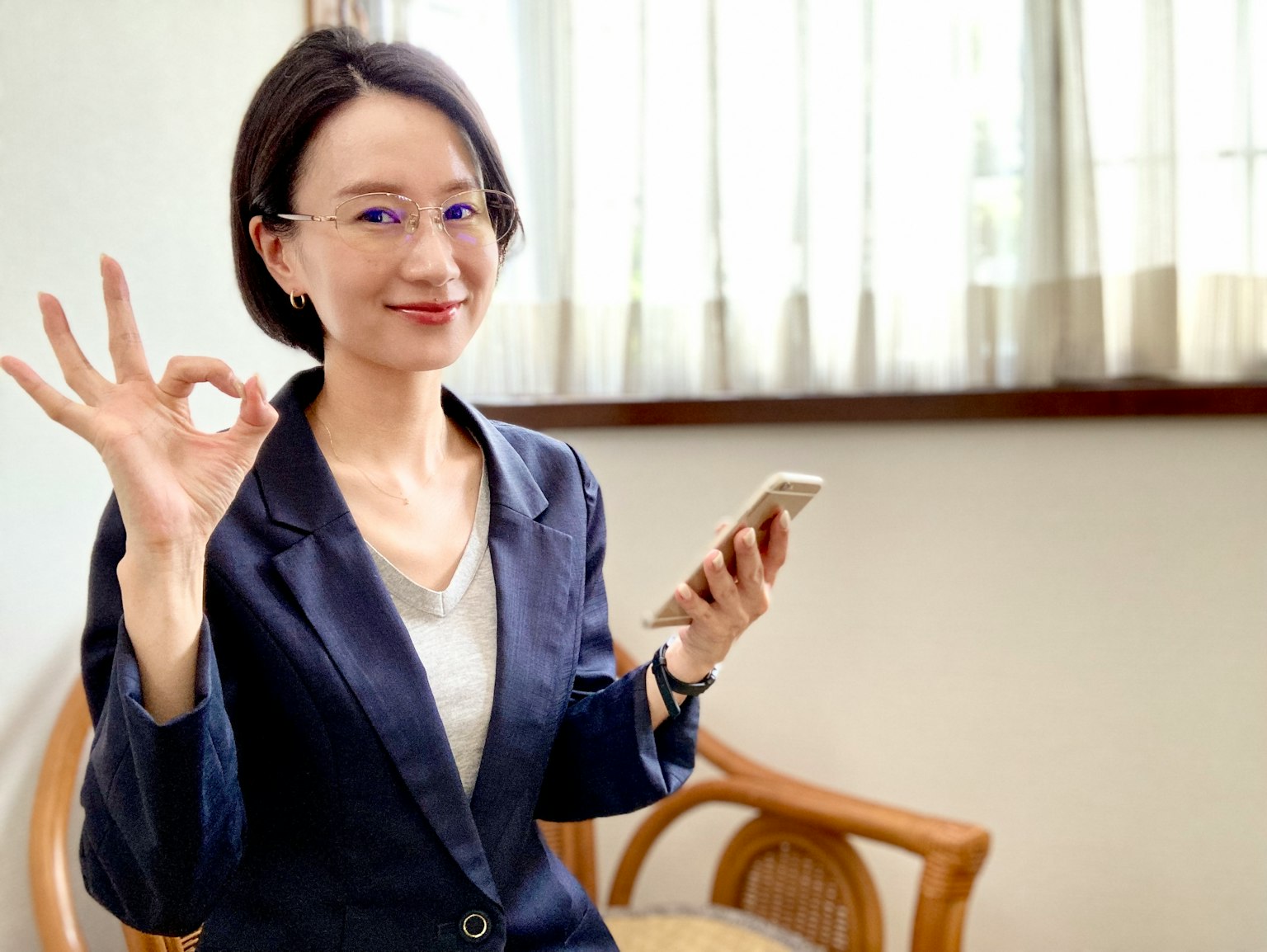 一位穿着商务套装的女性手持智能手机做出OK手势