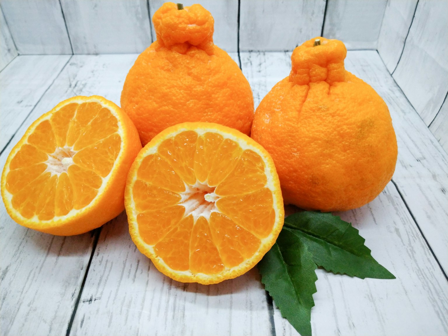Tre arance con una tagliata a metà che mostra la polpa arancione brillante e foglie verdi