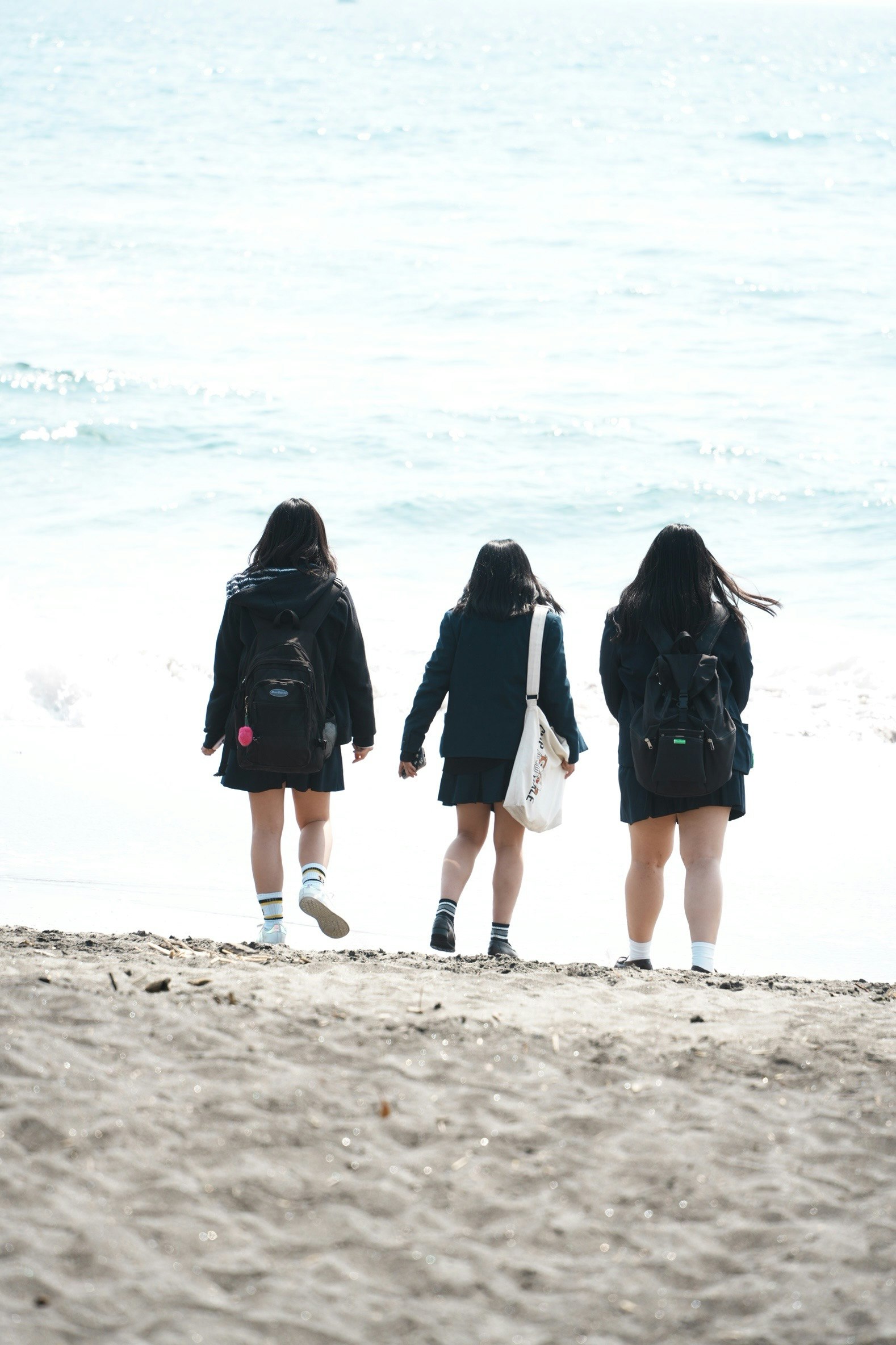 海辺で背を向けて歩く三人の女性たち