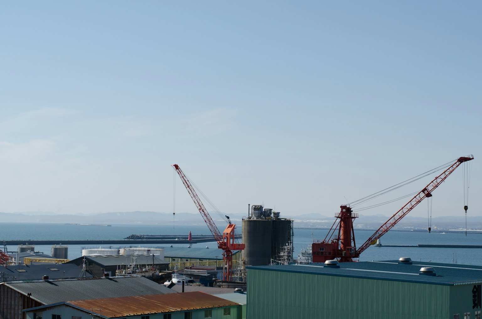 Vista de grúas en un puerto con edificios industriales y el mar