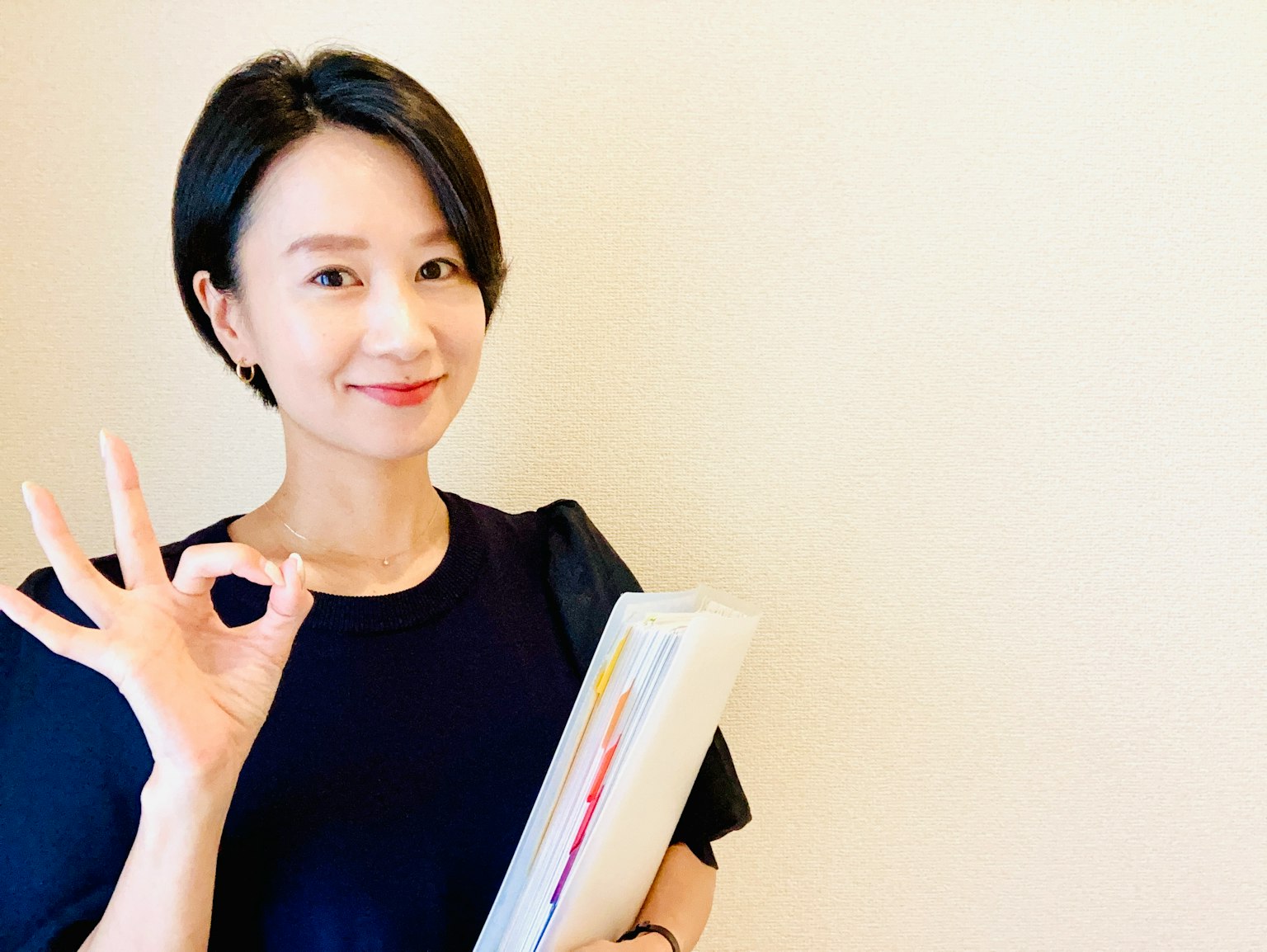 一位女性微笑着用手做出OK手势，同时手里拿着一个文件夹