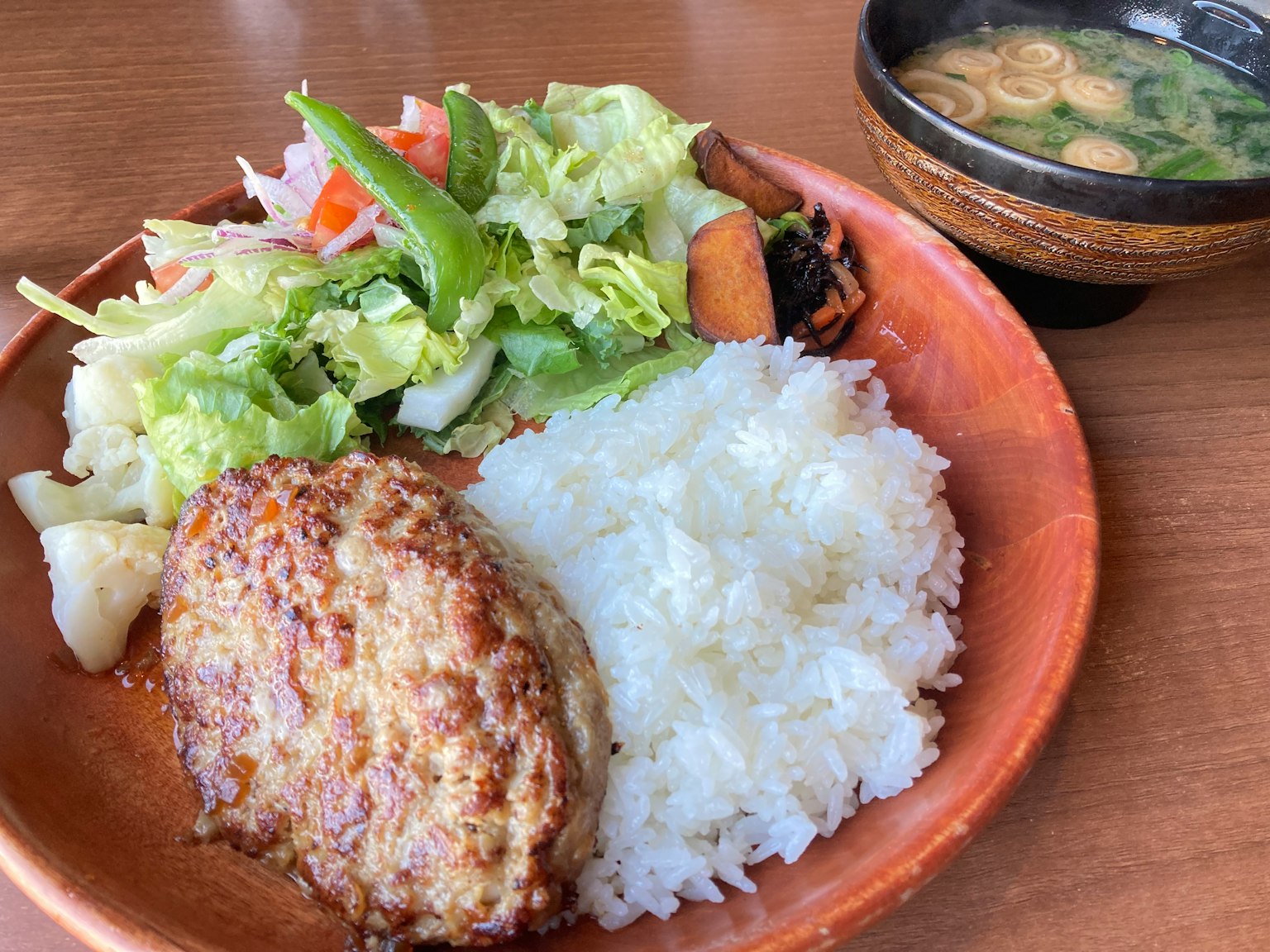 A plate with hamburger steak white rice fresh salad and miso soup
