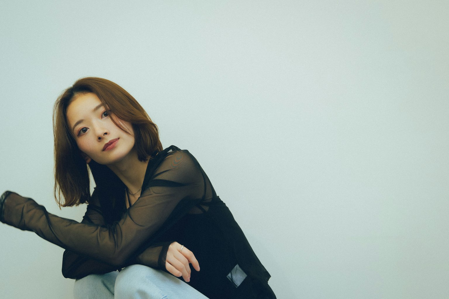 坐在简单背景前的女性肖像穿着黑色上衣和牛仔裤头发披肩