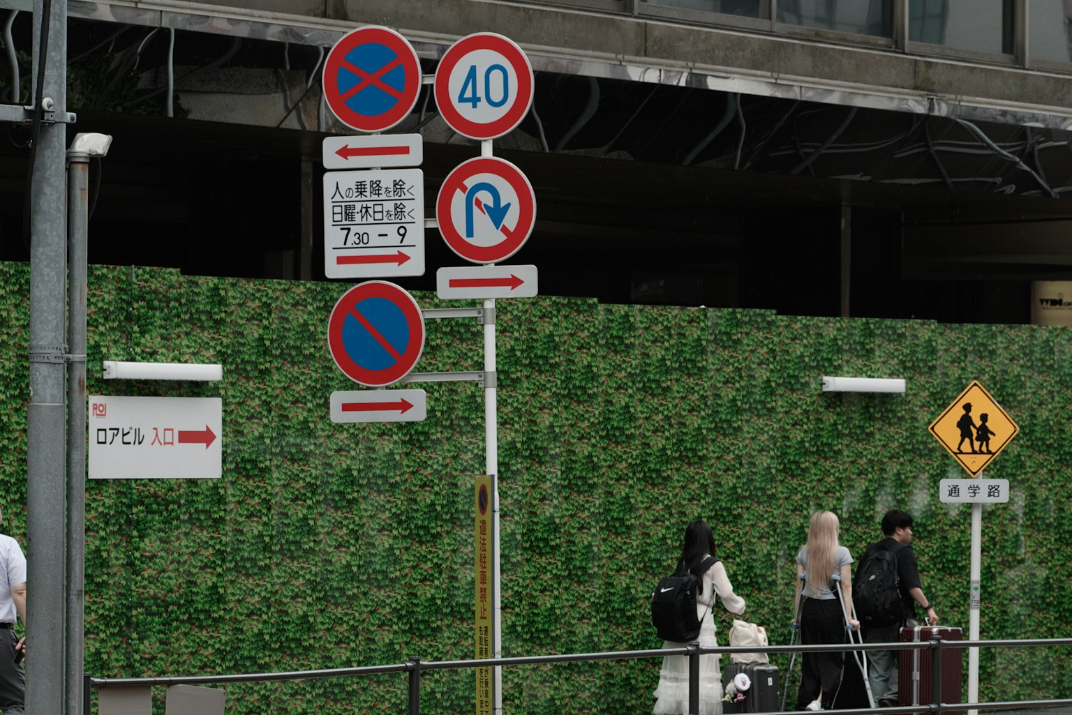 Señales de tráfico frente a una pared verde con peatones