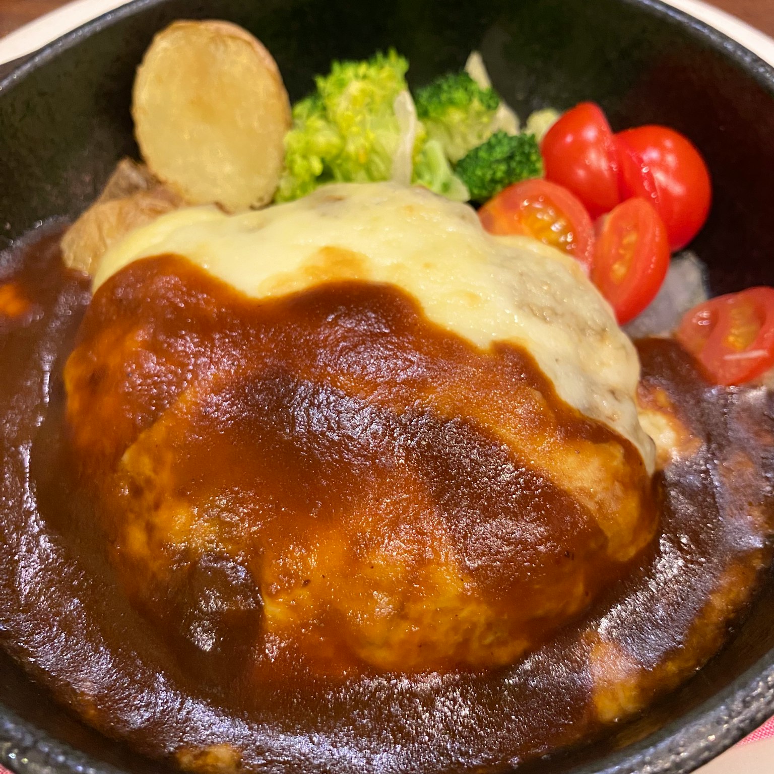 A hamburger steak topped with melted cheese and rich demi-glace sauce served with vegetables