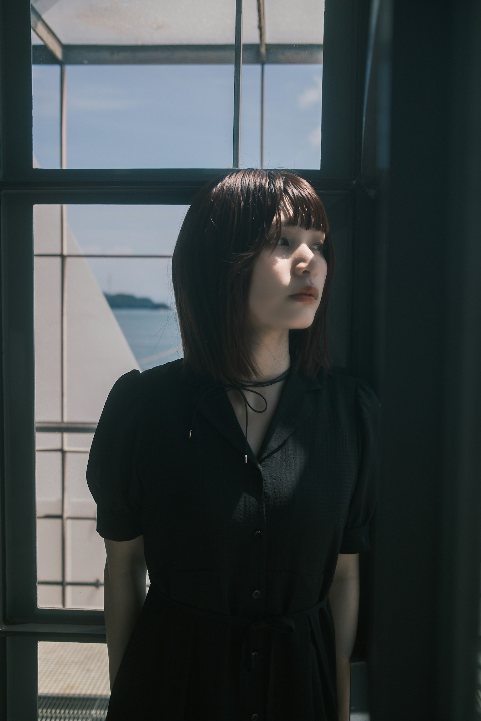 窓の近くに立つ女性のポートレート 黒いドレスを着ている 自然光が差し込む
