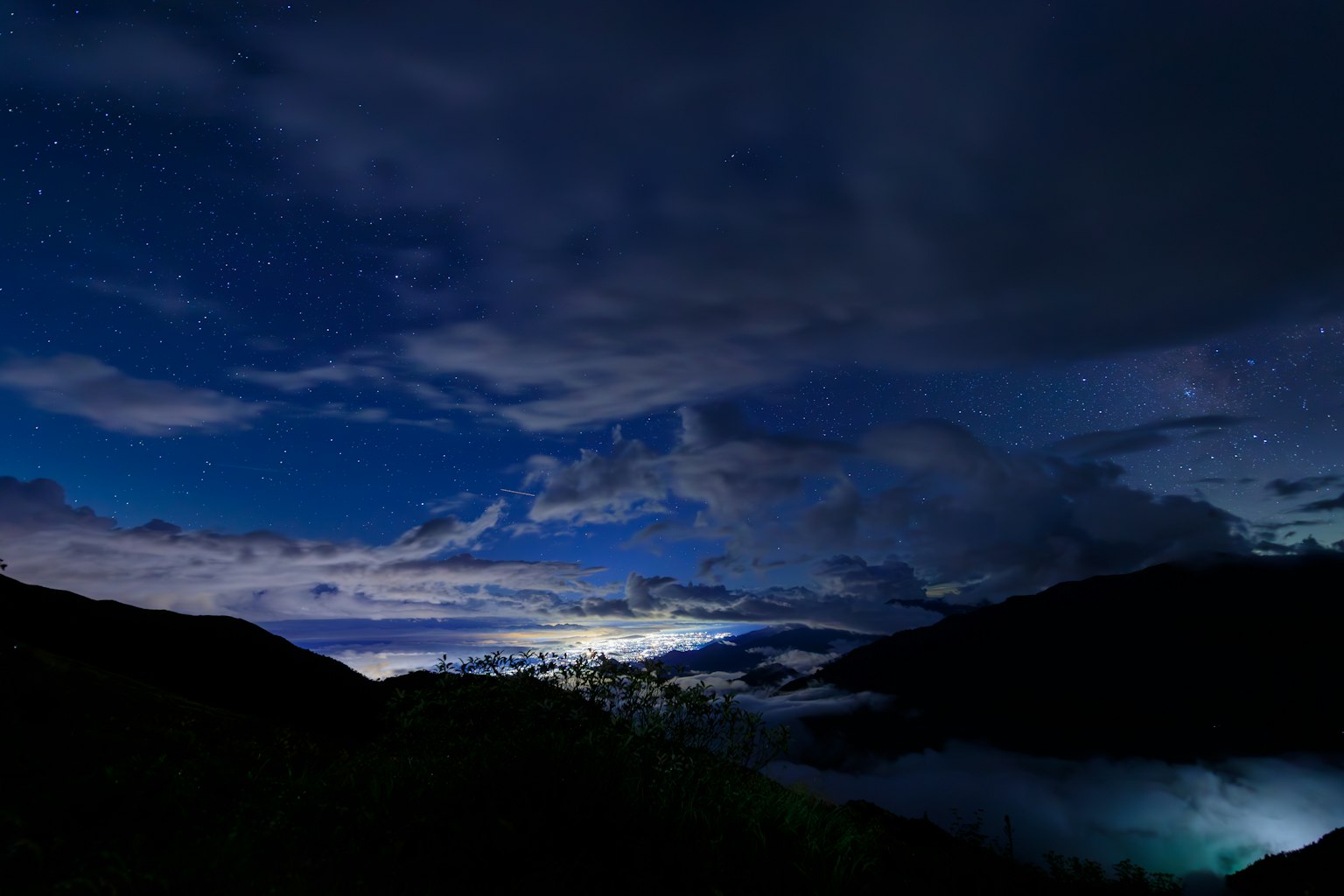 Cielo nocturno lleno de estrellas y nubes sobre un paisaje montañoso
