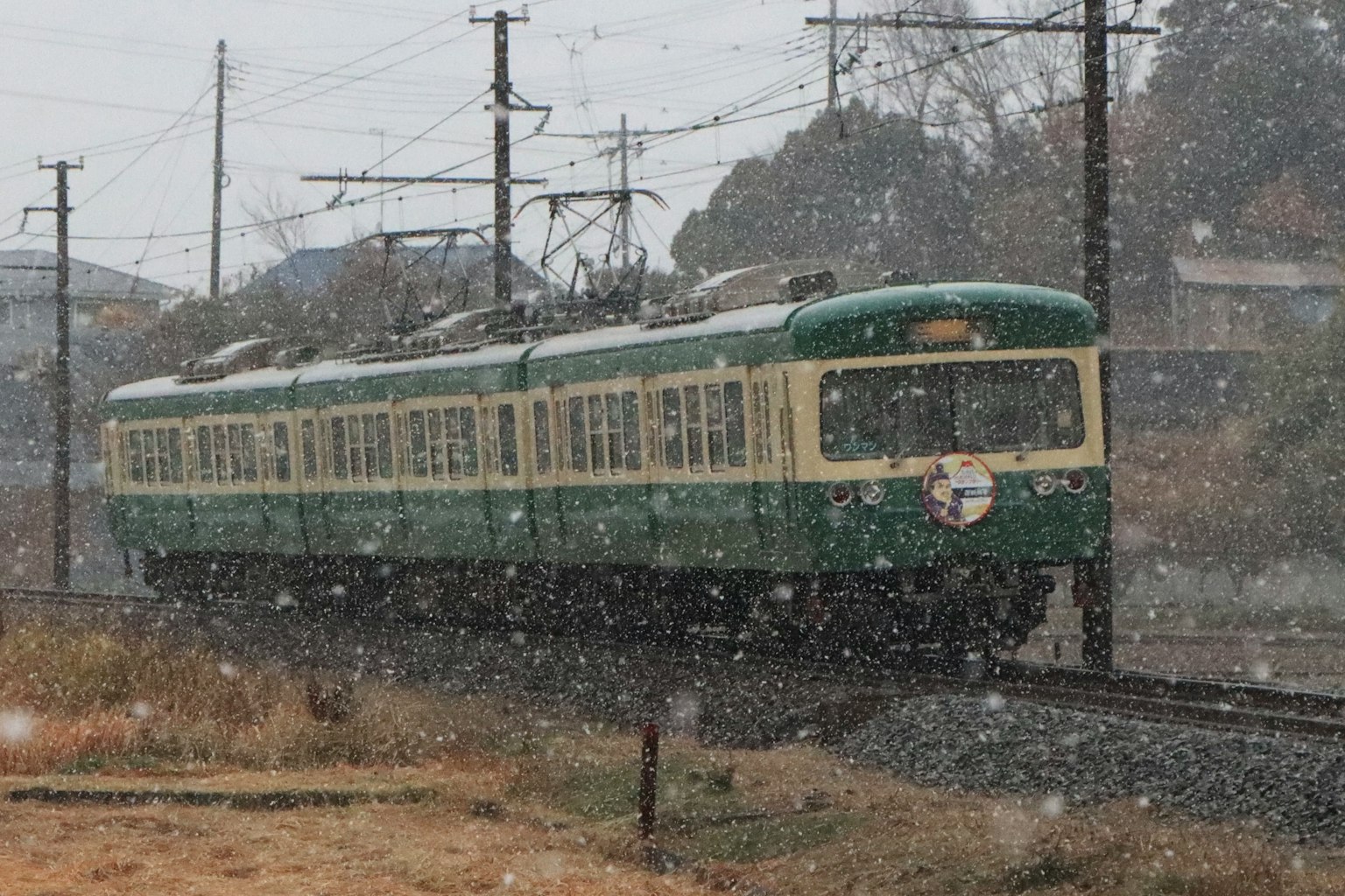 Un tren verde y crema viajando por la nieve con líneas eléctricas al fondo